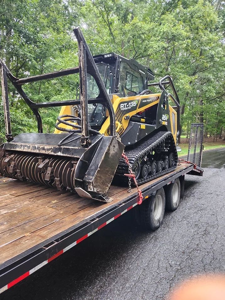 Yellow and black forestry mulcher on a trailer, ready for transport. Tracks, protective cage, and mulching head are visible.