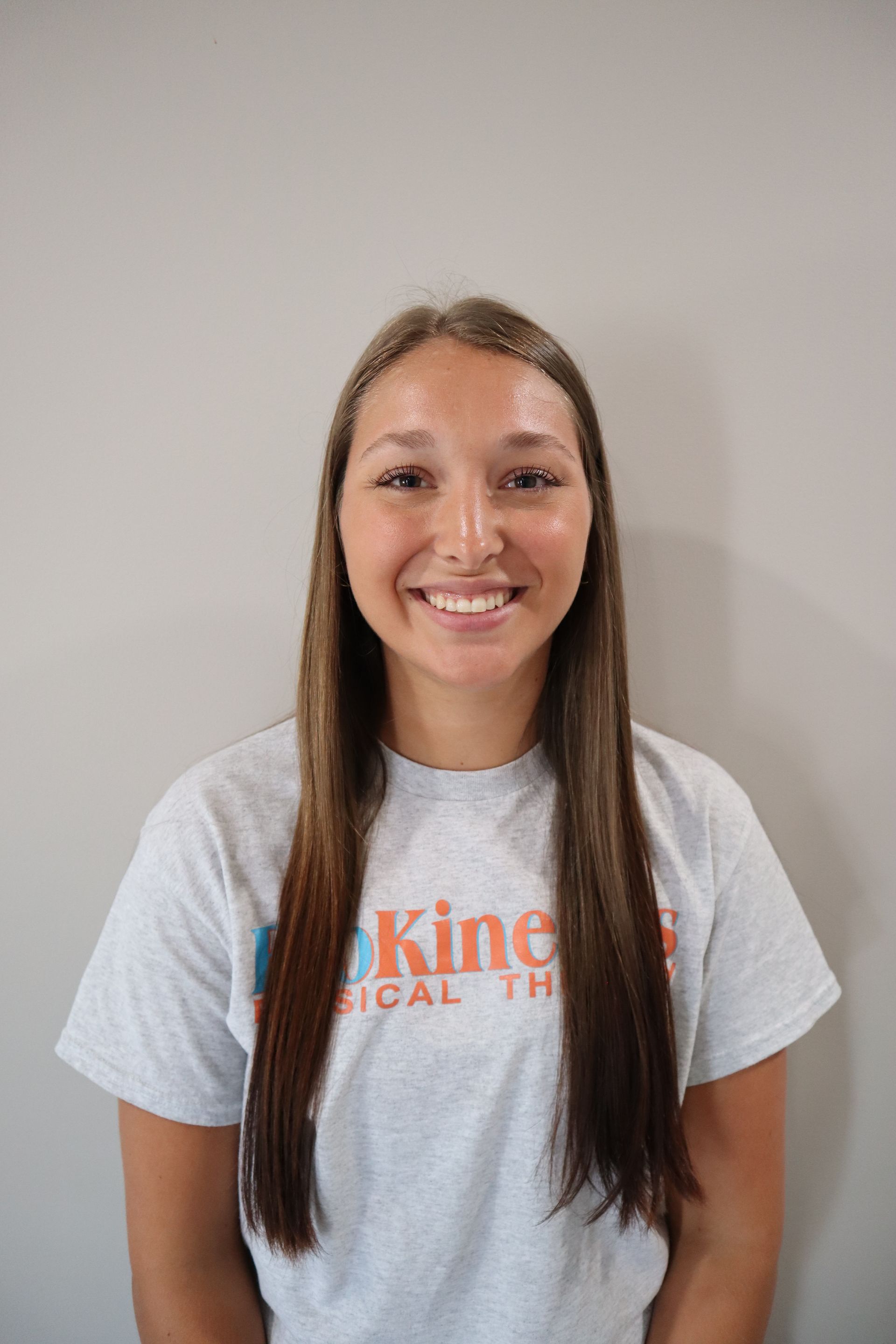 A woman with long hair is wearing a white t-shirt and smiling.