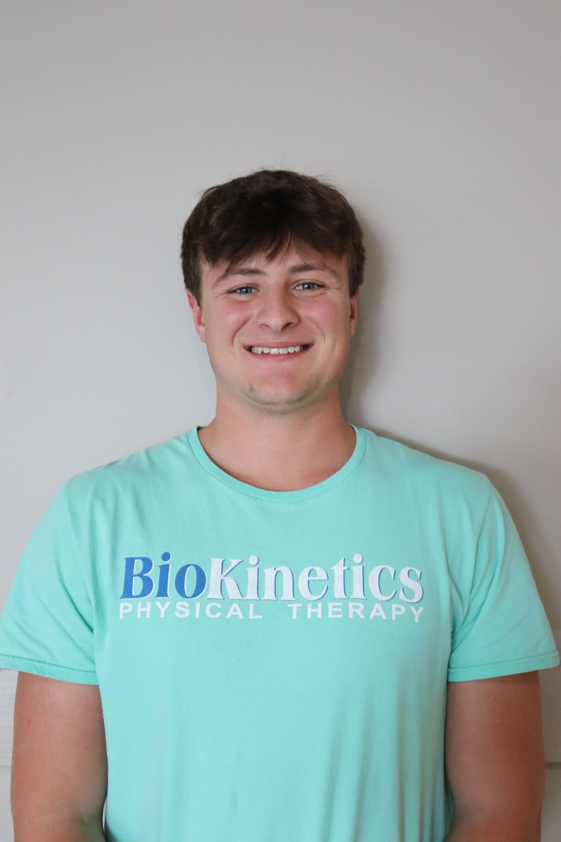 A young man is wearing a blue t-shirt that says biokinetics physical therapy.