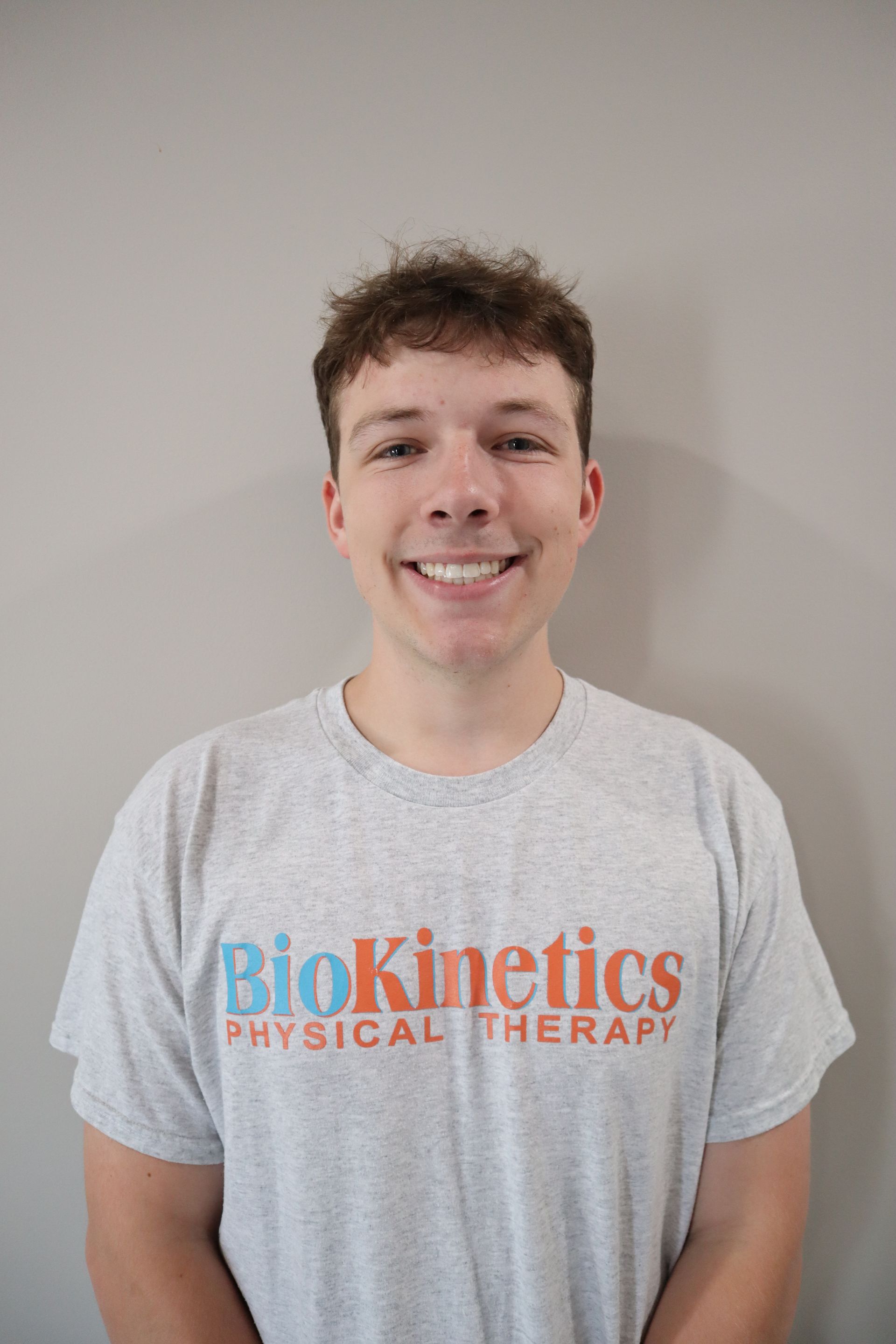 A young man wearing a biokinetics physical therapy t-shirt is smiling for the camera.