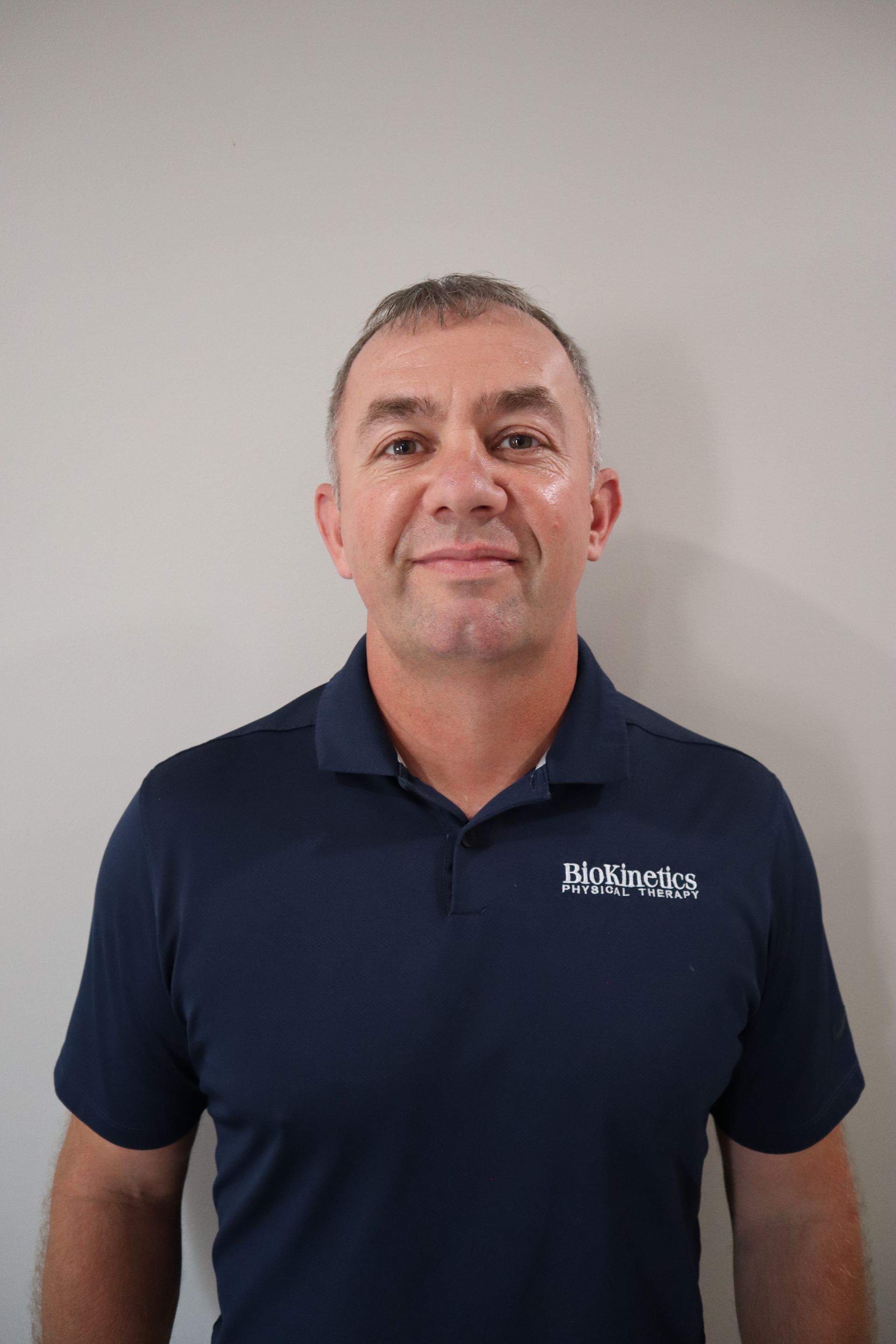 A man in a blue shirt is standing in front of a white wall.