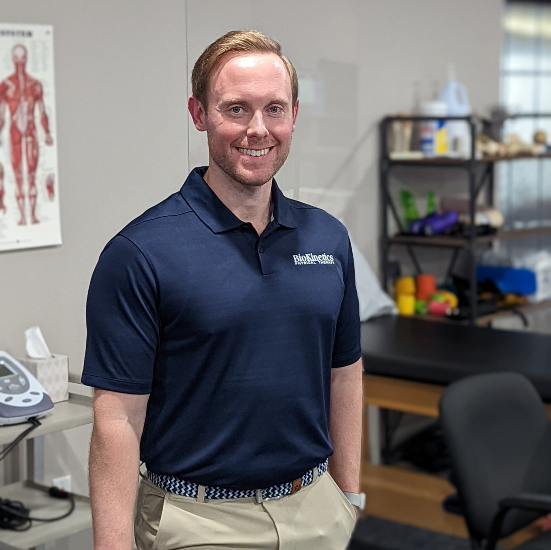 A man in a blue shirt and khaki pants is standing in a room.