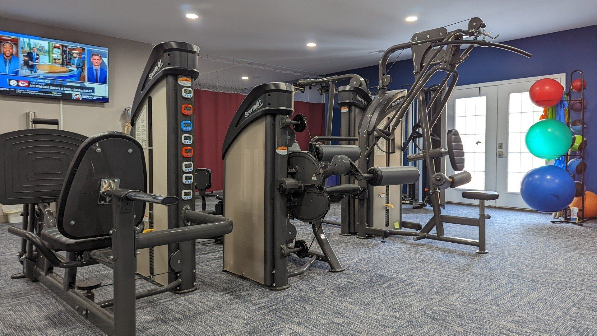 A gym with a lot of exercise equipment and a television on the wall.