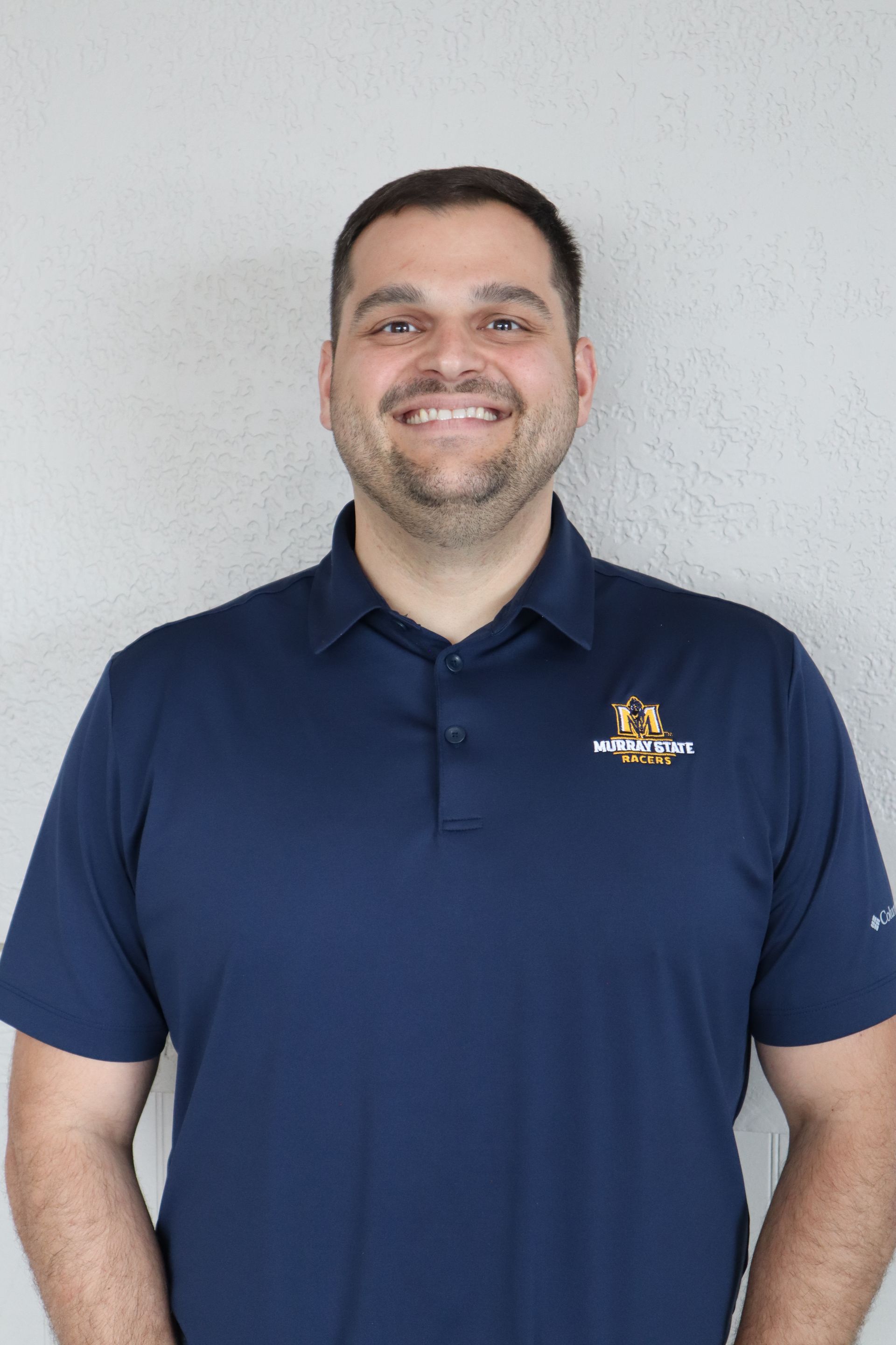 A man wearing a blue polo shirt is smiling for the camera.