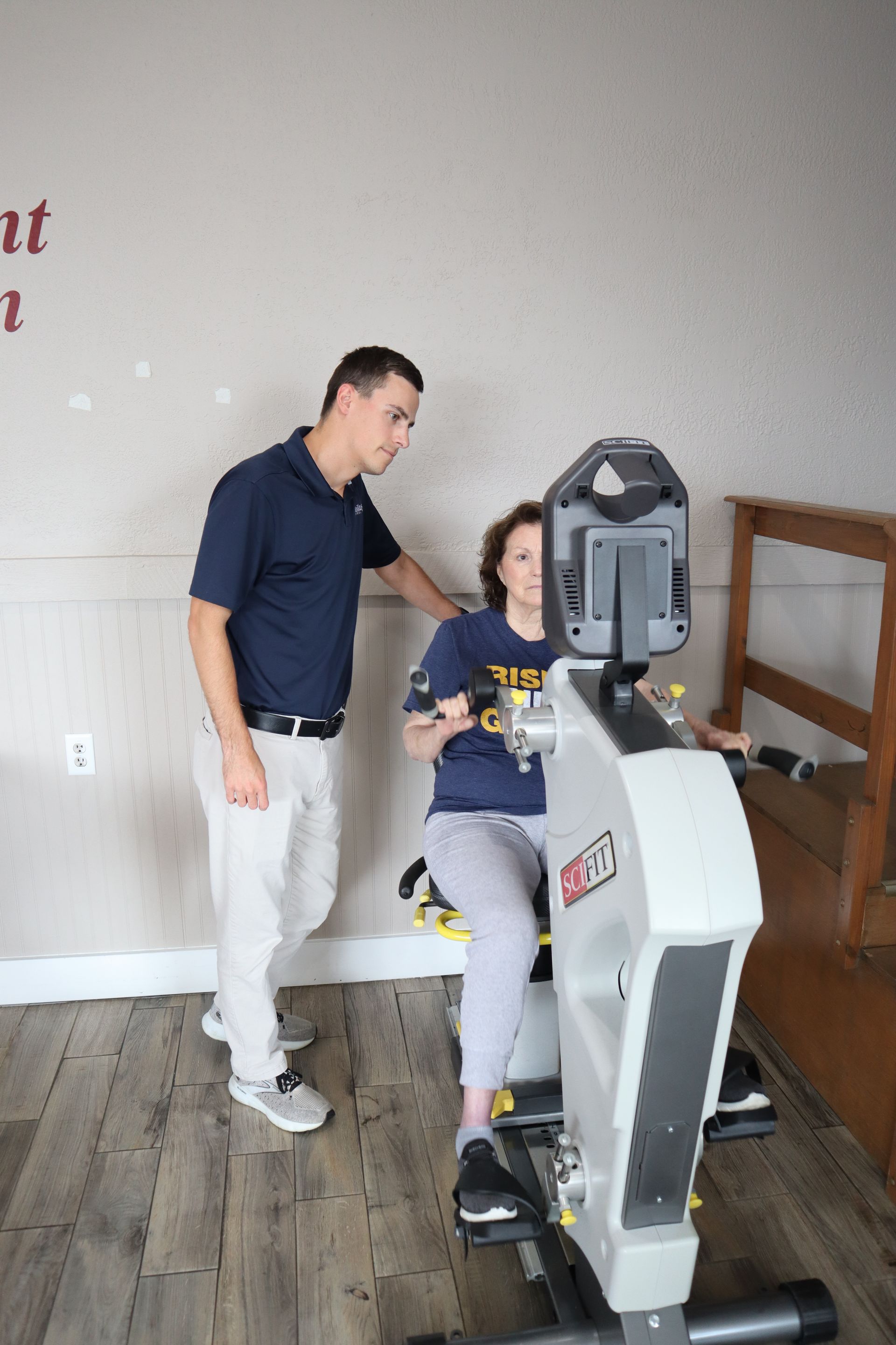 A man is helping a woman ride an exercise bike.