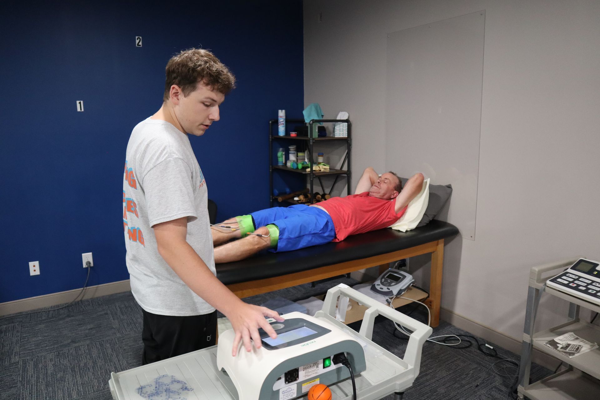 A man is standing next to a person laying on a bed.