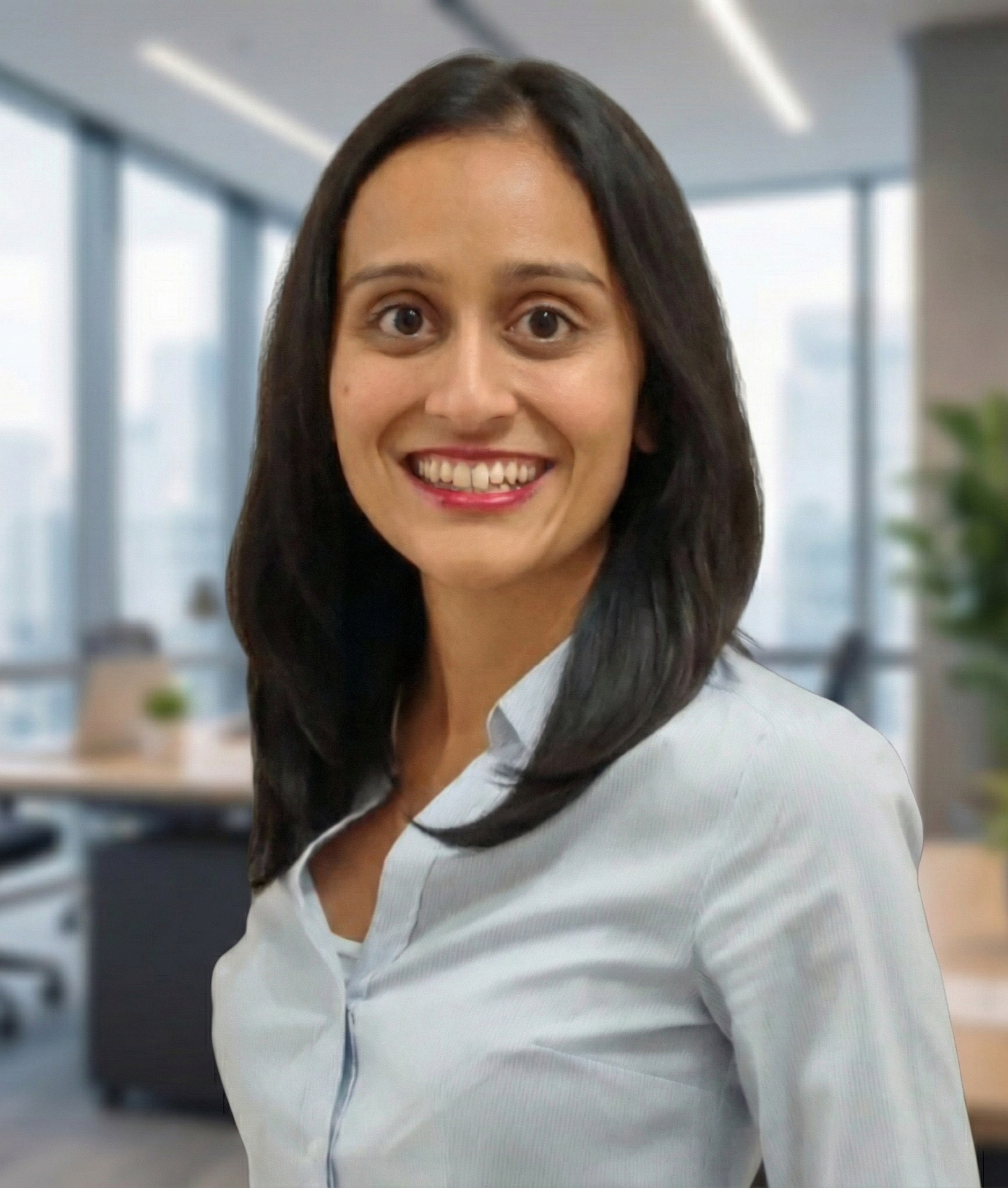 Woman smiling in office setting; wearing a light blue button-down shirt.