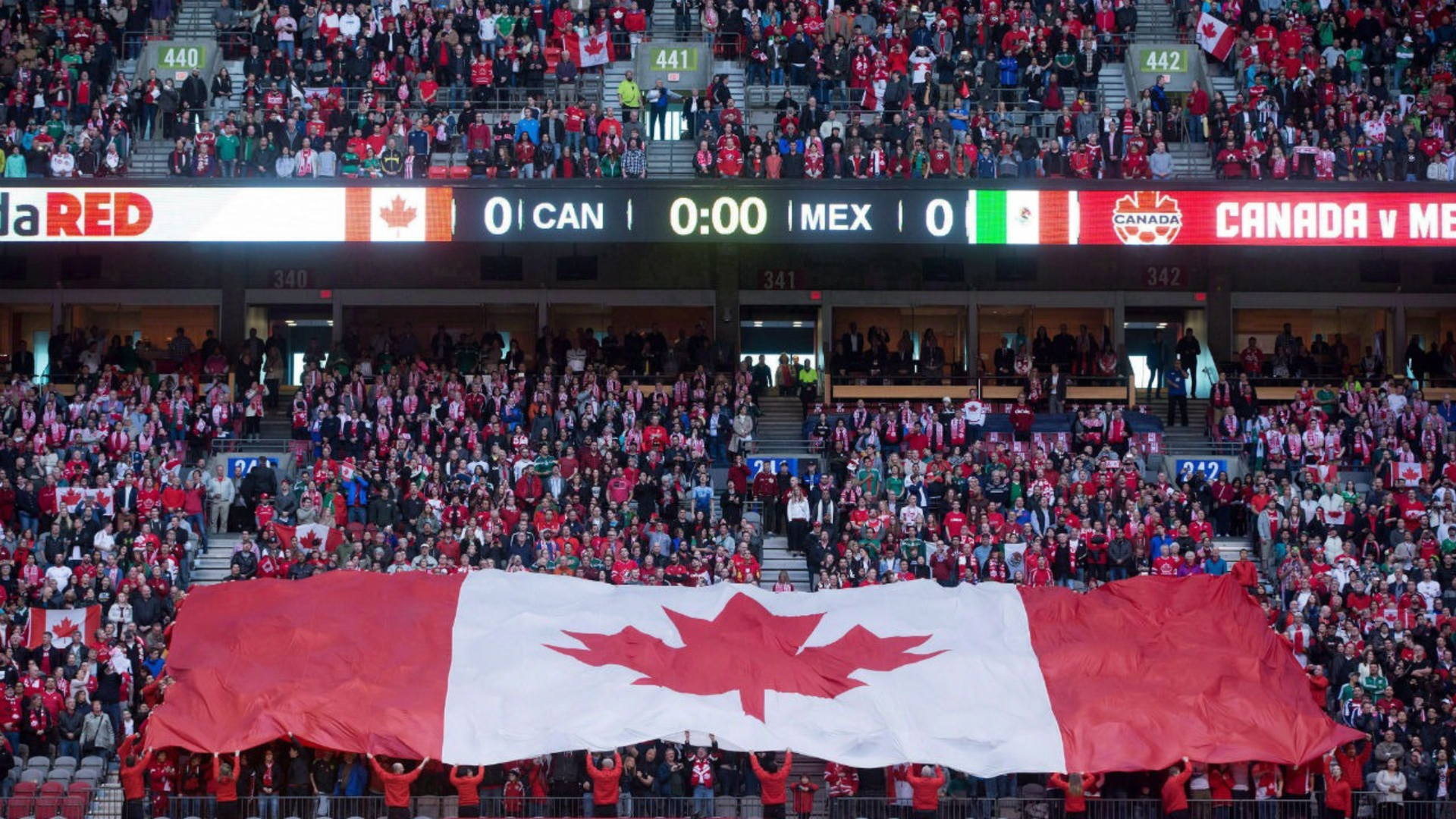 Crowd in stadium holding a large Canadian flag during a Canada vs Mexico soccer match