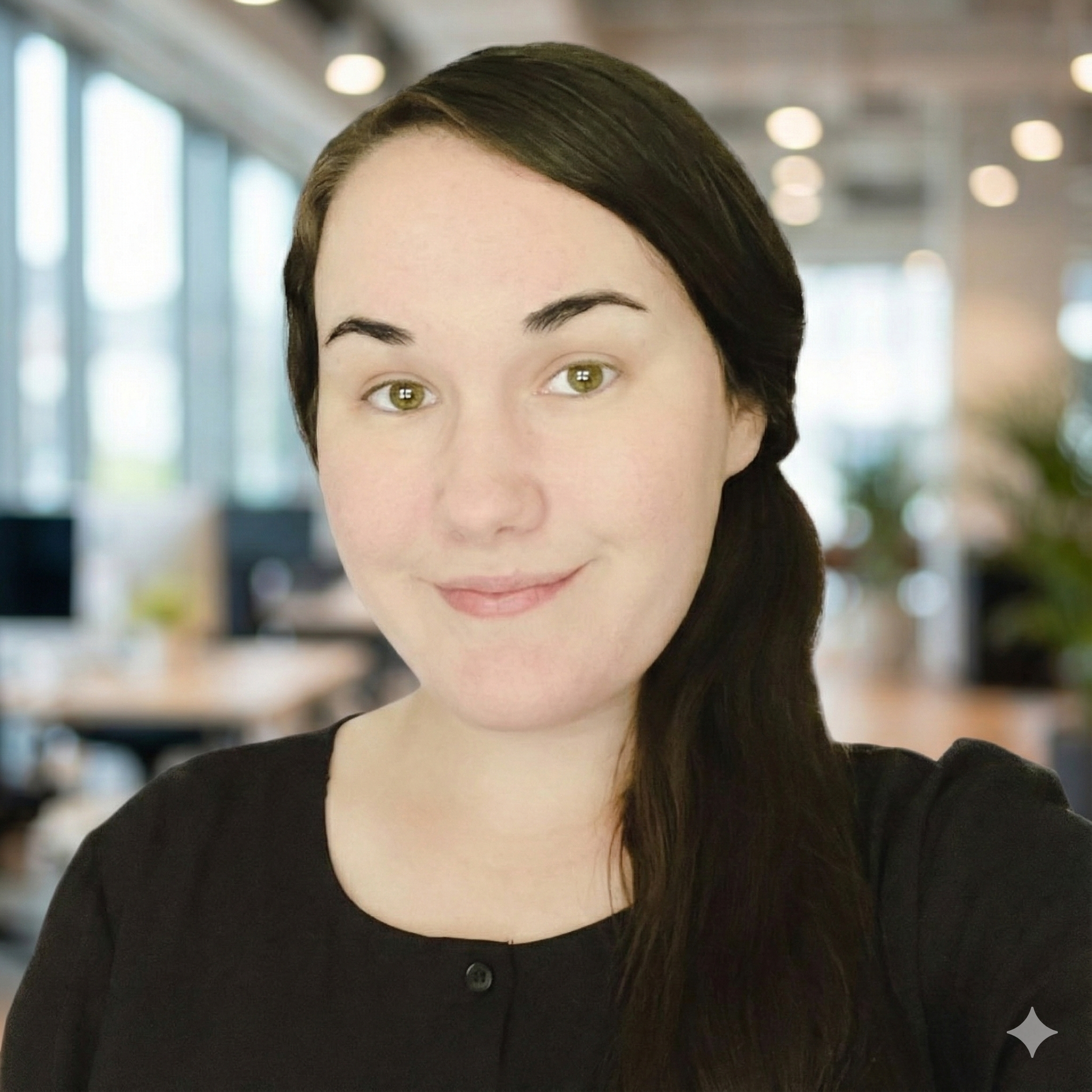 Woman with dark hair in a low ponytail, smiling in an office setting, wearing a black top.
