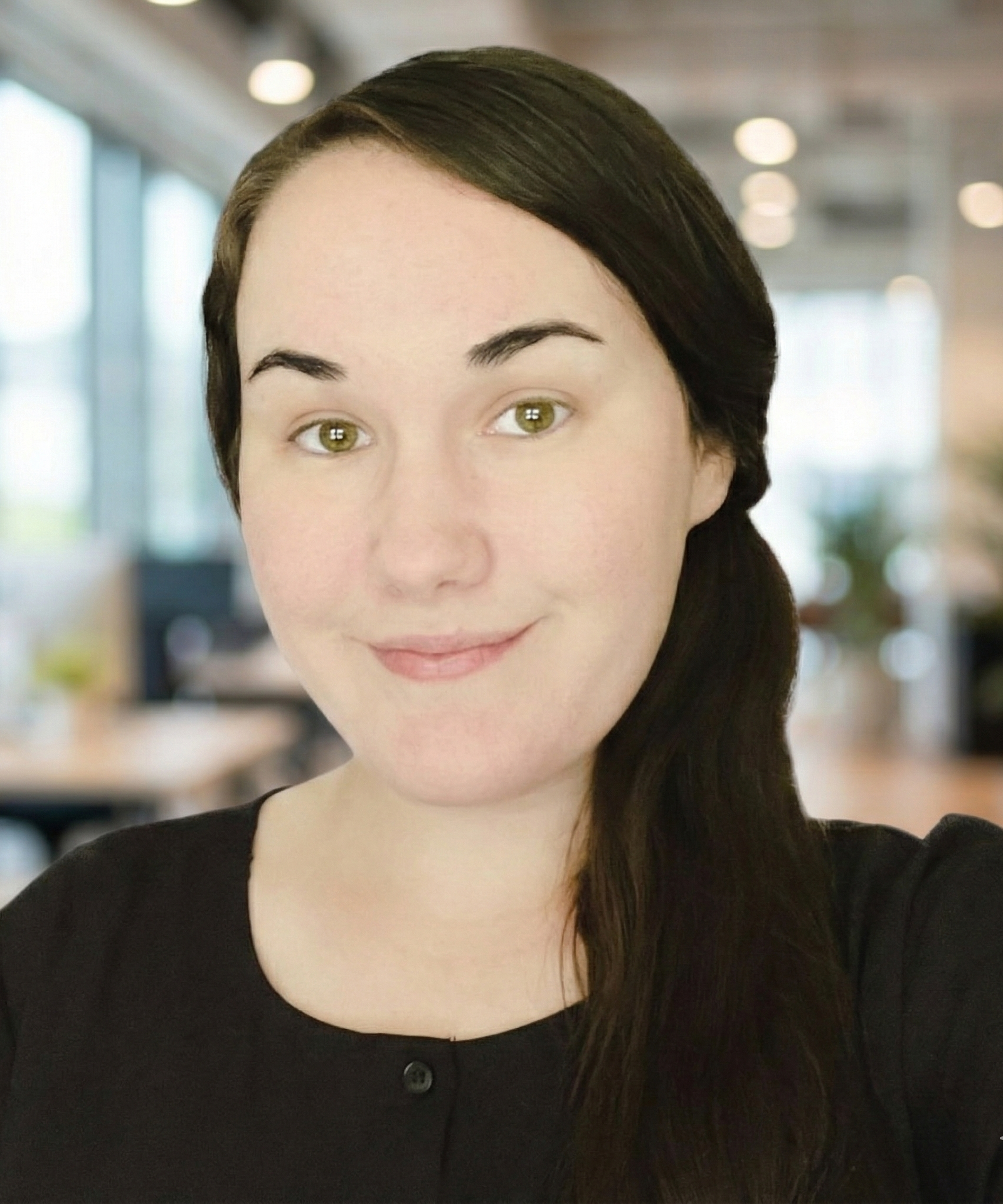 Woman with dark hair smiles, wearing a black shirt in an office.