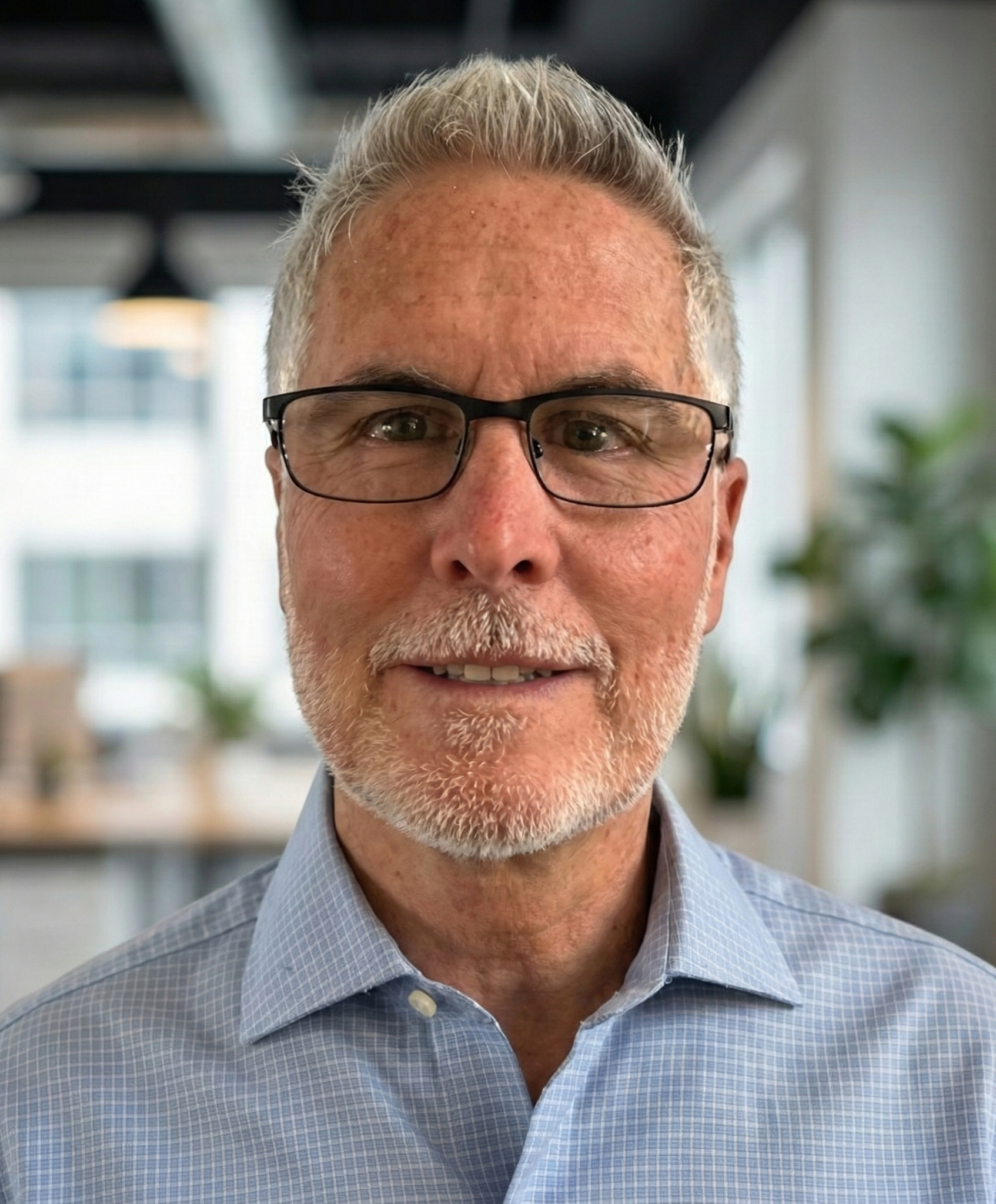 Man with glasses and grey hair smiling in a blue shirt indoors.