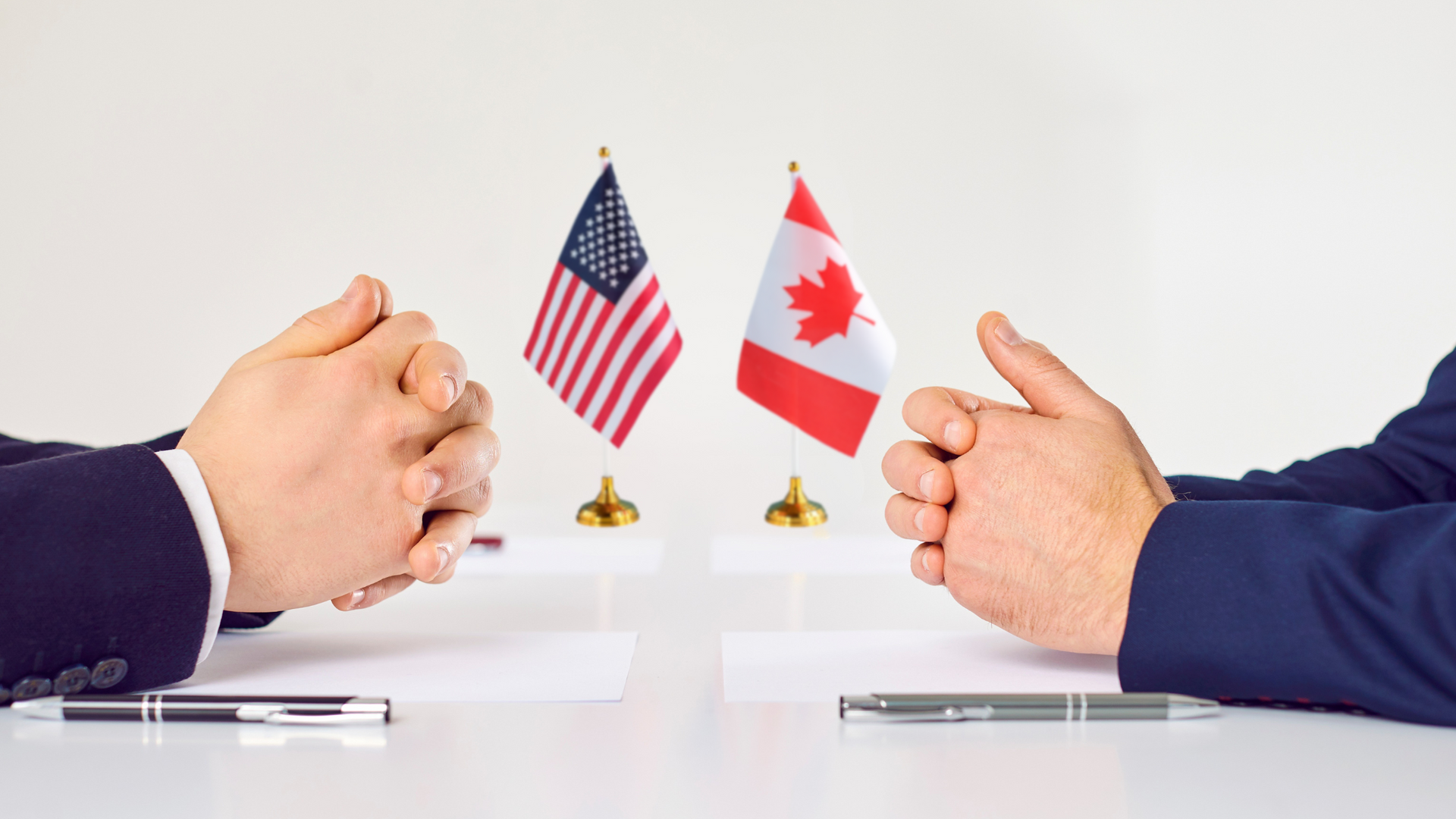 Two people's hands clasped in front of US and Canadian flags, indicating negotiation.