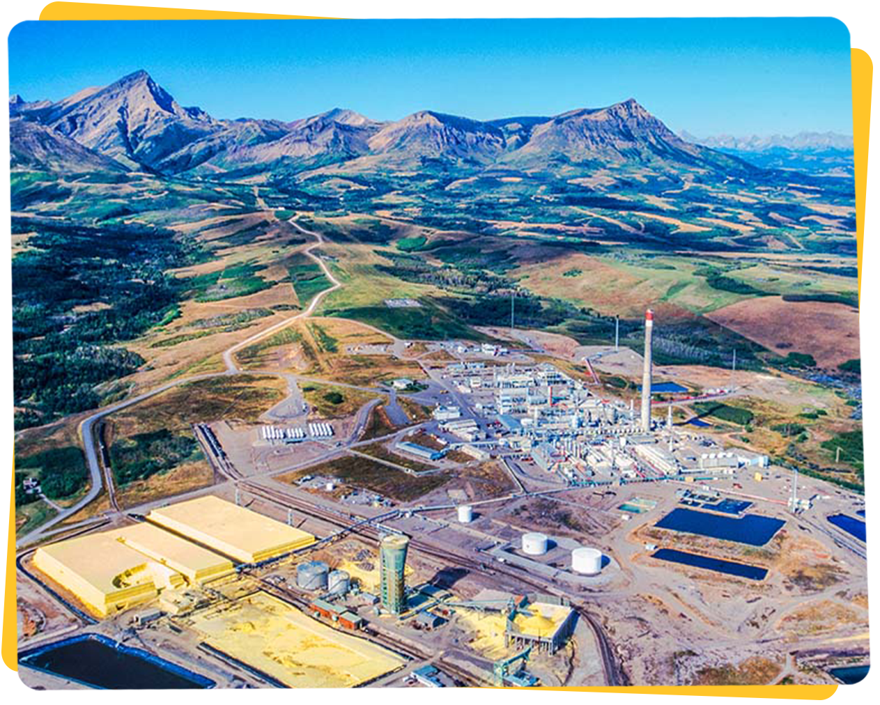 Aerial view of an industrial facility with mountains in the background and yellow structures in the foreground.