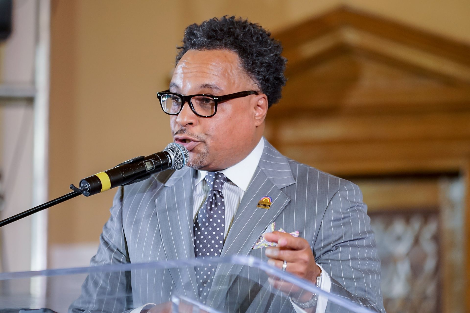 A man in a suit and tie is standing at a podium speaking into a microphone.