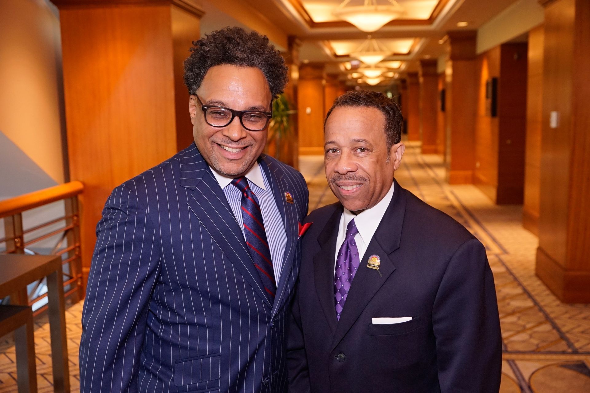 Two men in suits and ties are posing for a picture in a hallway.