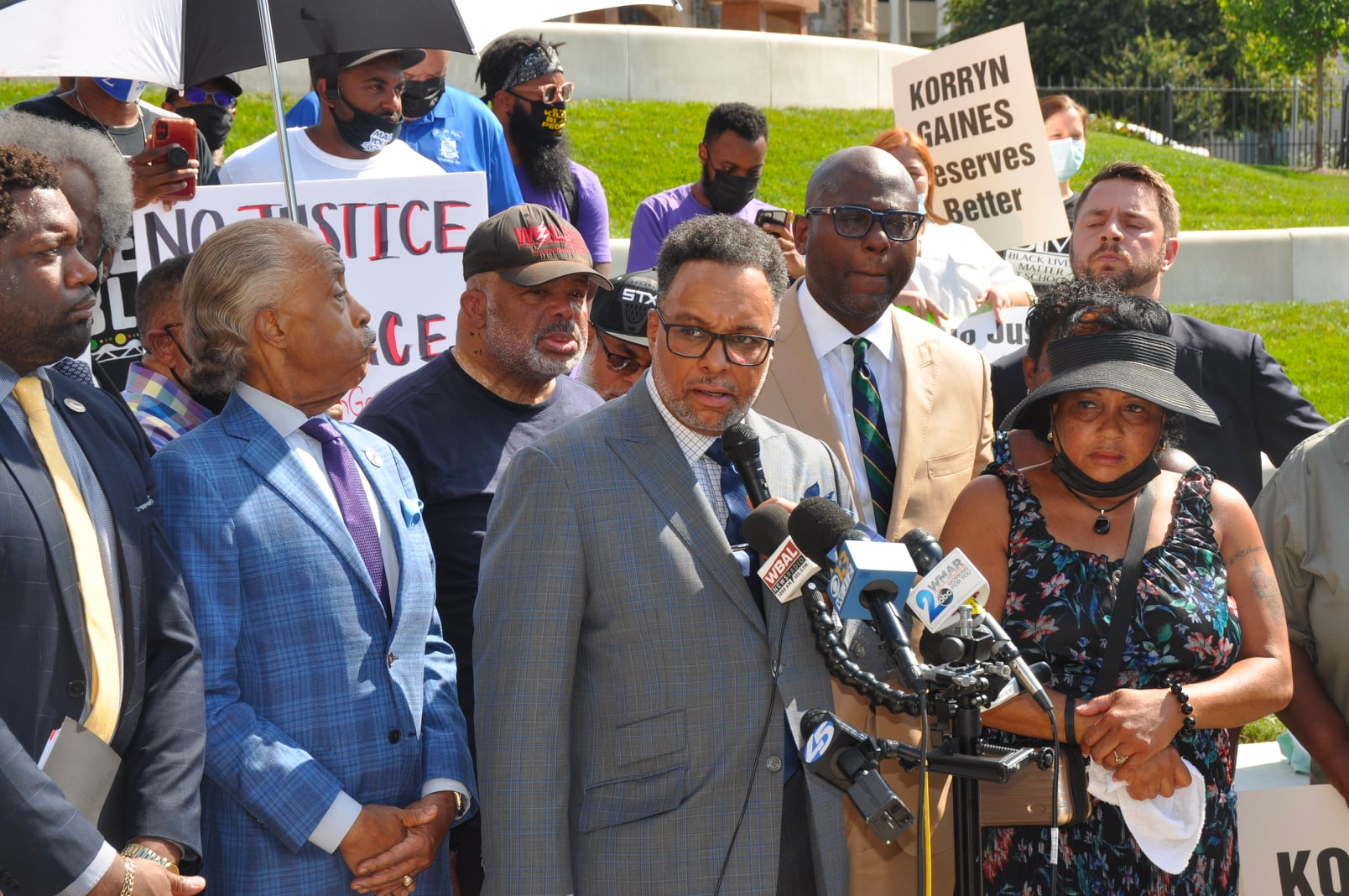 A man in a suit is standing in front of a group of people holding signs.