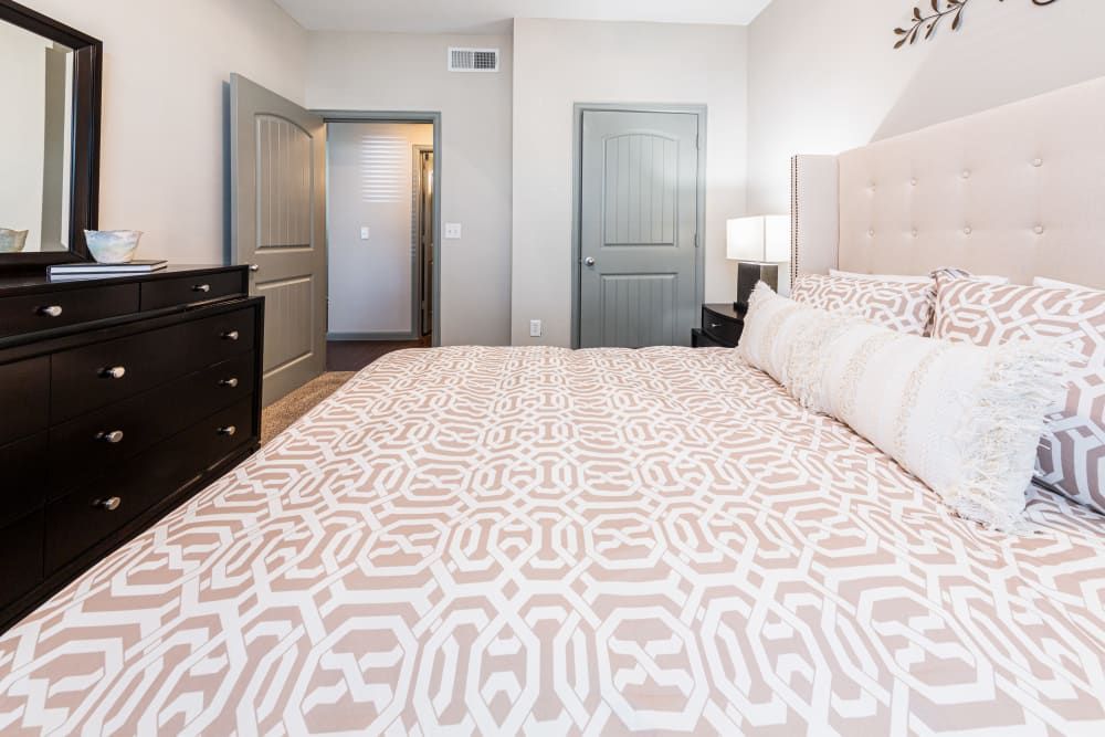 a bedroom with a bed, dresser, and mirror at Marquis at Katy in Katy, TX.