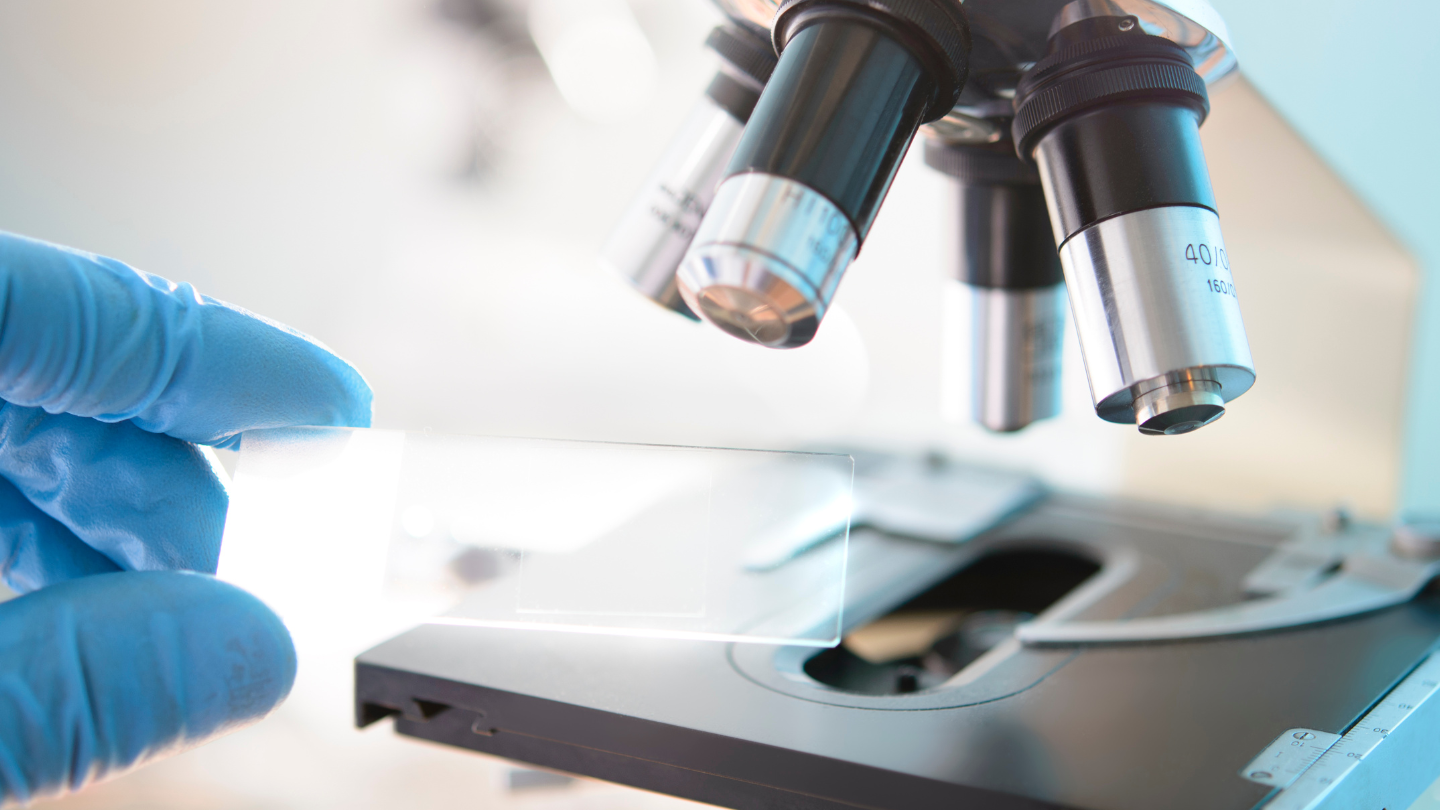 A person is holding a slide in front of a microscope.