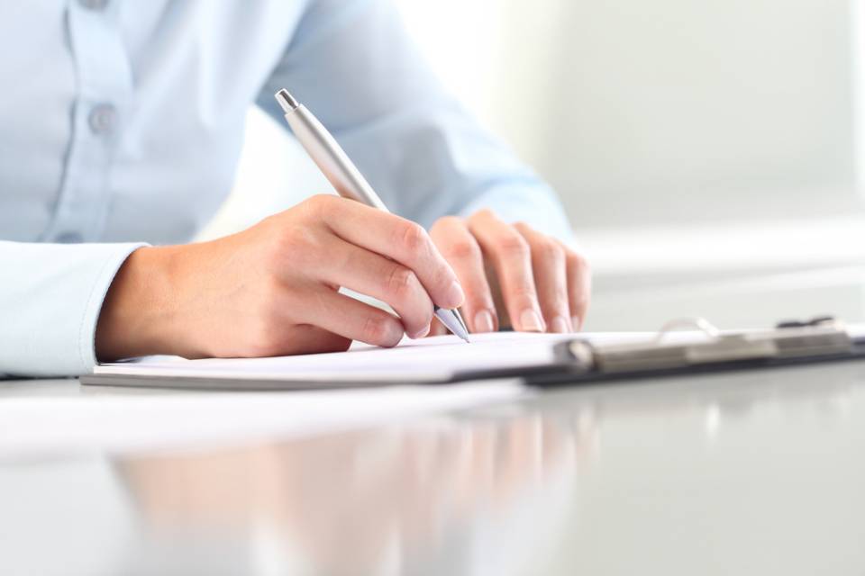 Una persona sta scrivendo su un blocco per appunti con una penna.