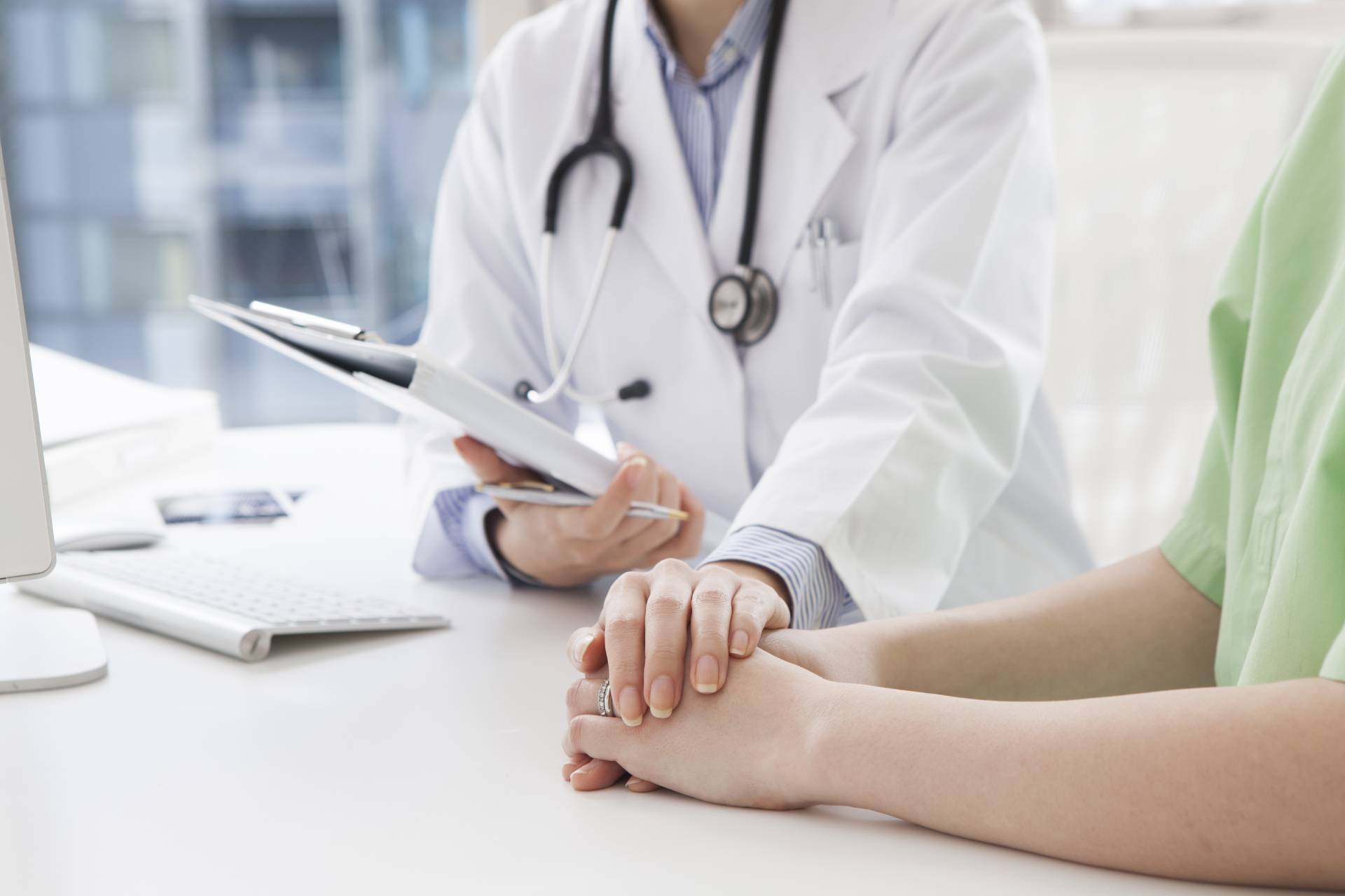 Un medico tiene la mano di un paziente mentre guarda un blocco per appunti.
