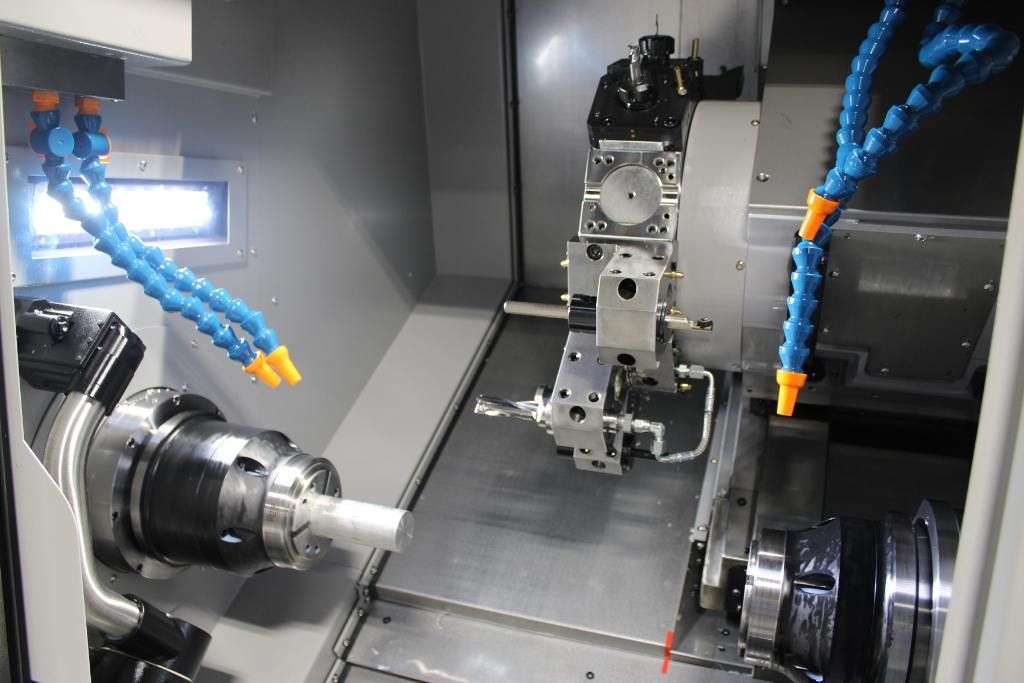 CNC machine with coolant hoses spraying metal part inside enclosure.