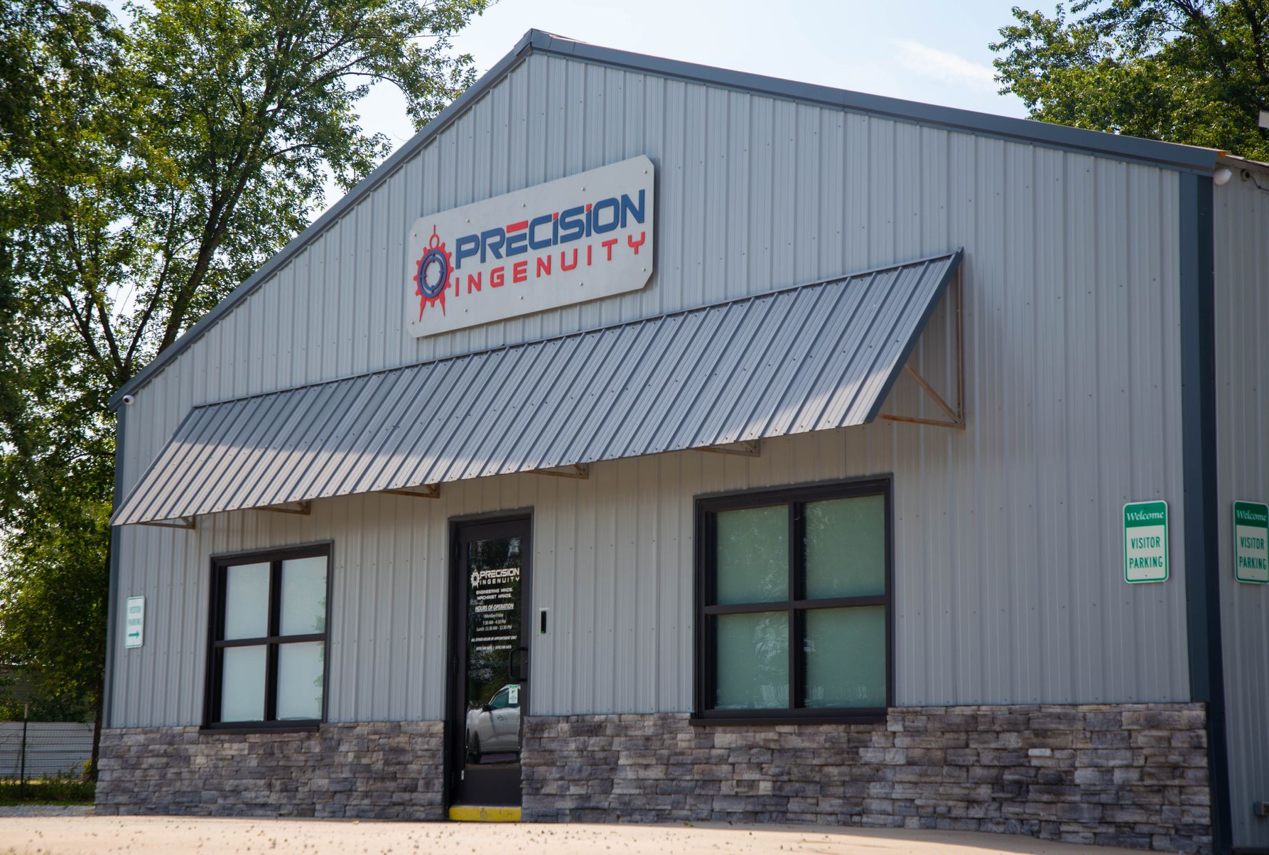 Exterior of Precision Ingenuity building with a grey metal facade, awning, and stone base.