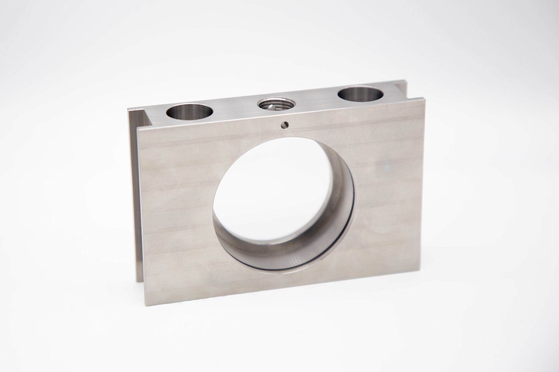 A rectangular metal block with a large central hole and two smaller holes on top.