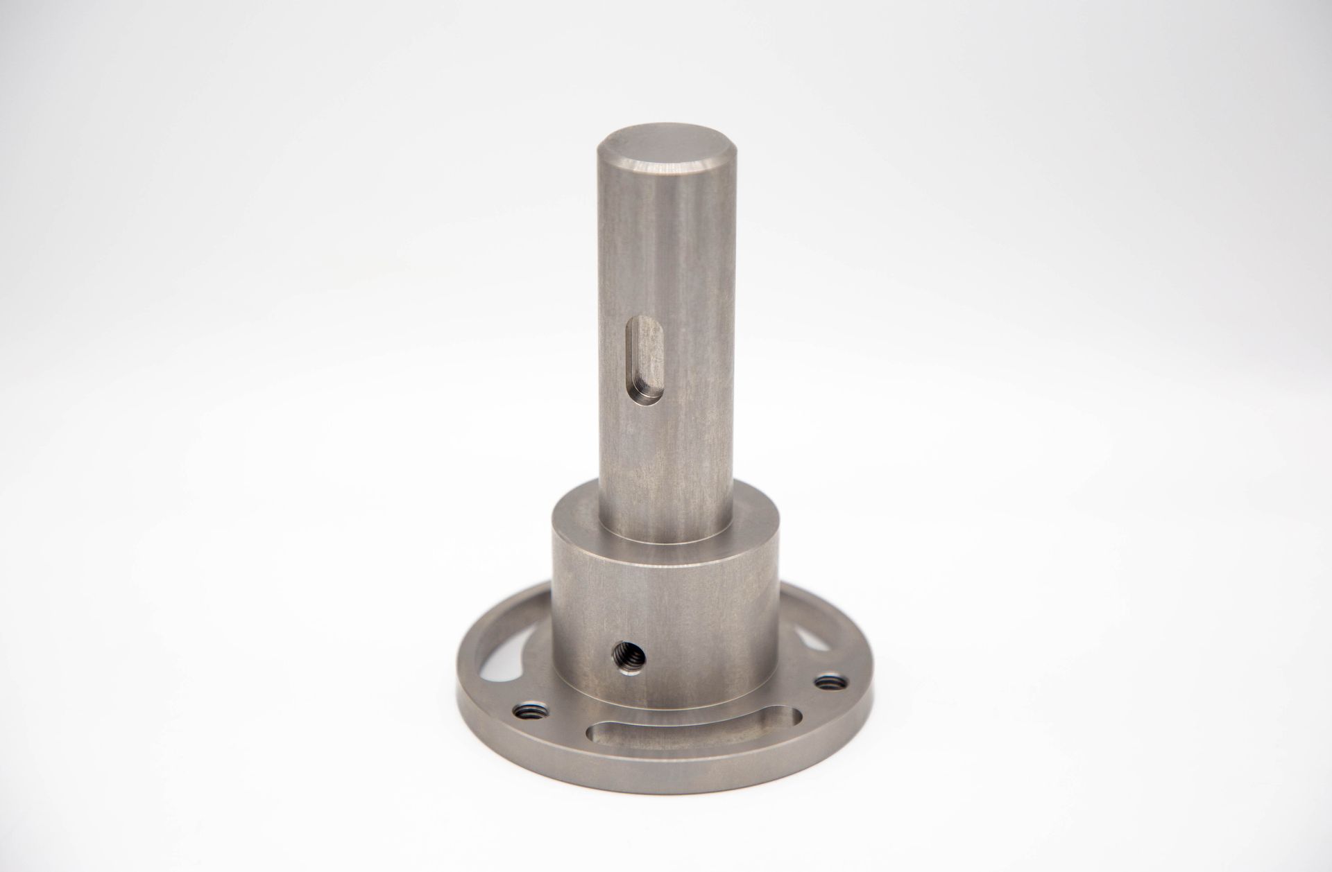 Metal machined part with cylindrical and circular features, including a central shaft and base with holes.