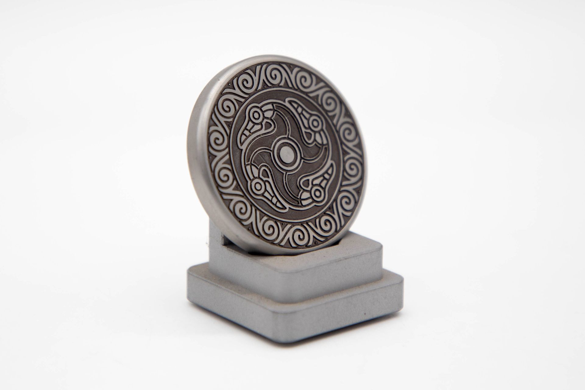 Silver coin with engraved Celtic design on a stone stand against a white backdrop.