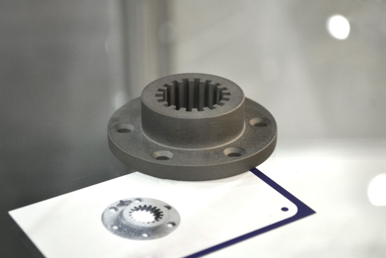 Metallic gear coupling with a circular flange, displayed on a white surface with a smaller component shown below.