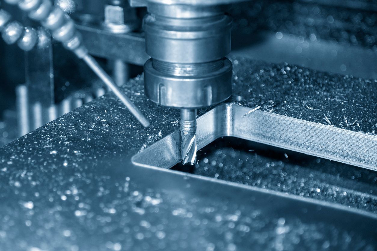 CNC milling machine cutting a metal part with a bit, generating shavings.
