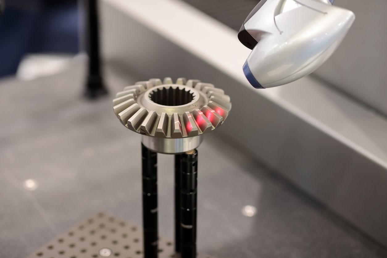 A gear being scanned by a robotic arm. Red laser dots appear on the gear's teeth.