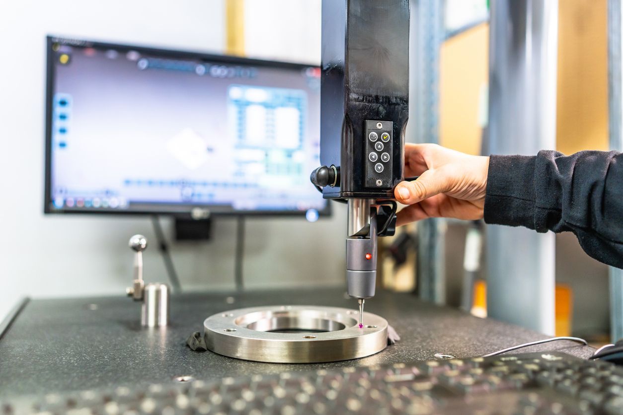 Person using a coordinate measuring machine to inspect a metal ring; monitor displays software interface.
