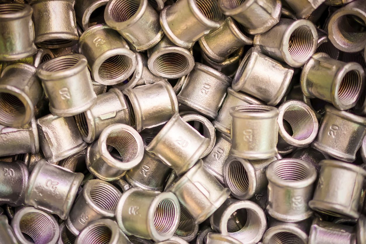 Pile of silver-colored pipe fittings with threaded interior, ready for use.