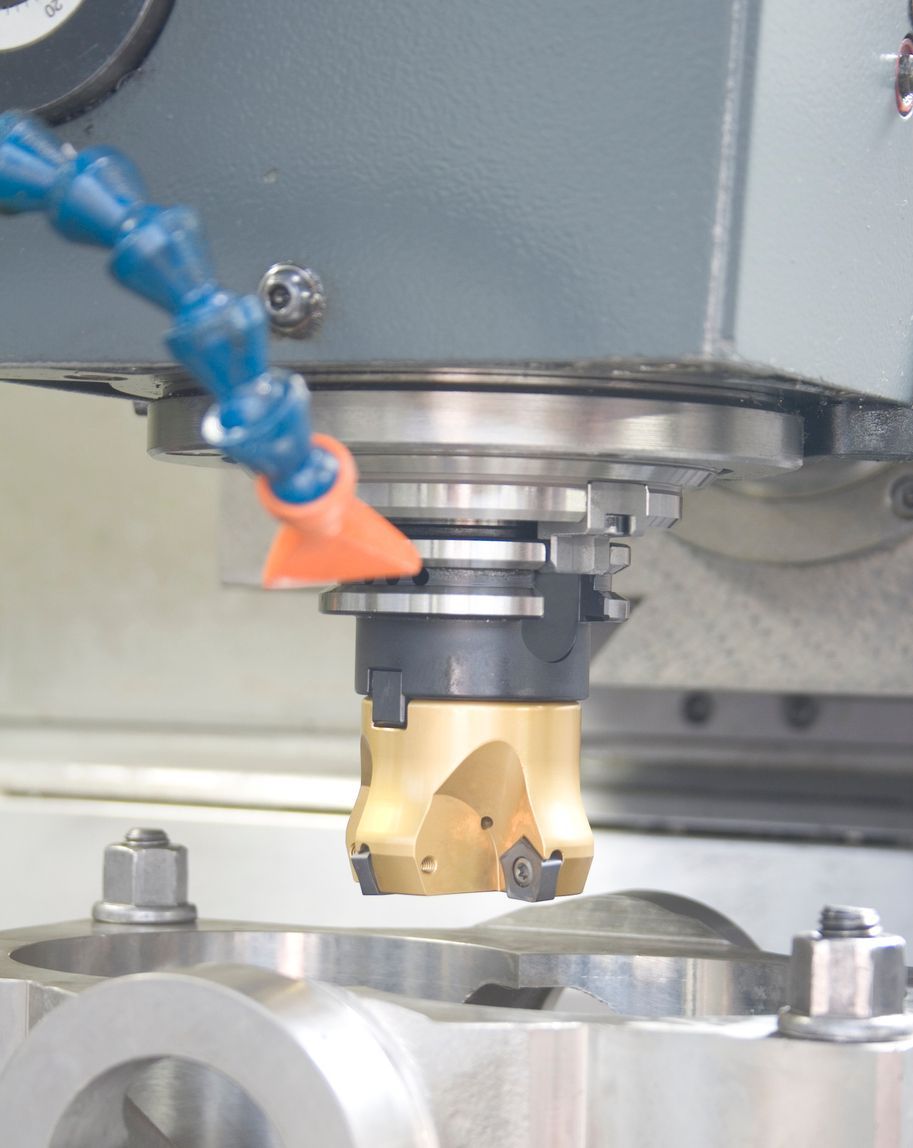 Close-up of a gold milling tool on a CNC machine with a blue coolant hose.
