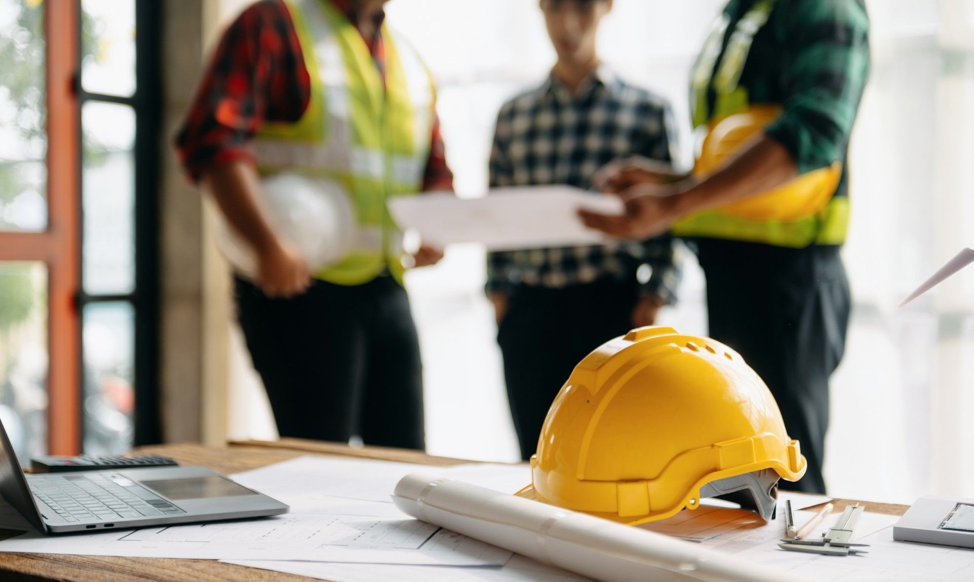 A group of construction workers are standing around a table with a hard hat.