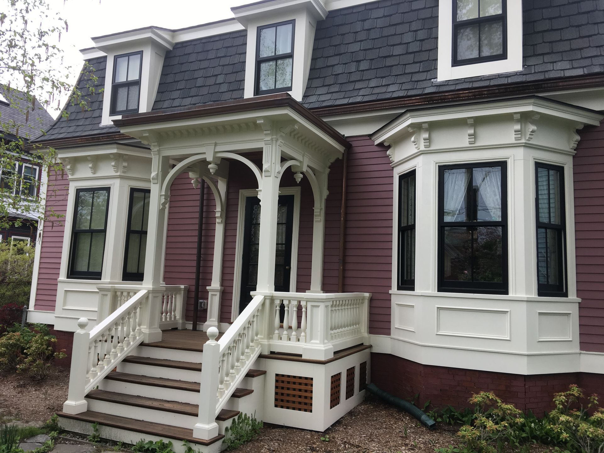 A pink house with a white porch and black windows