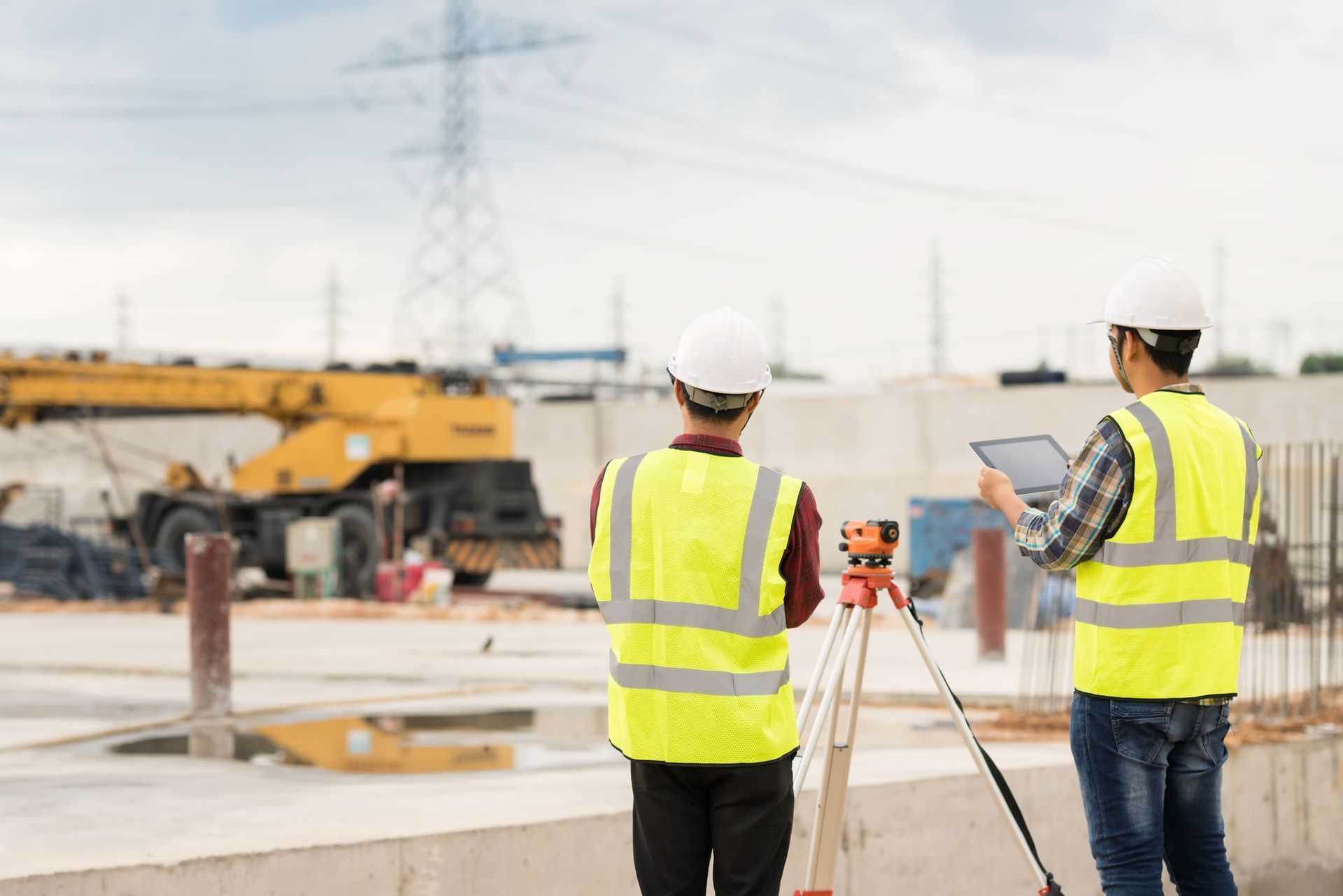 Two construction workers are standing on a construction site looking at a tablet.