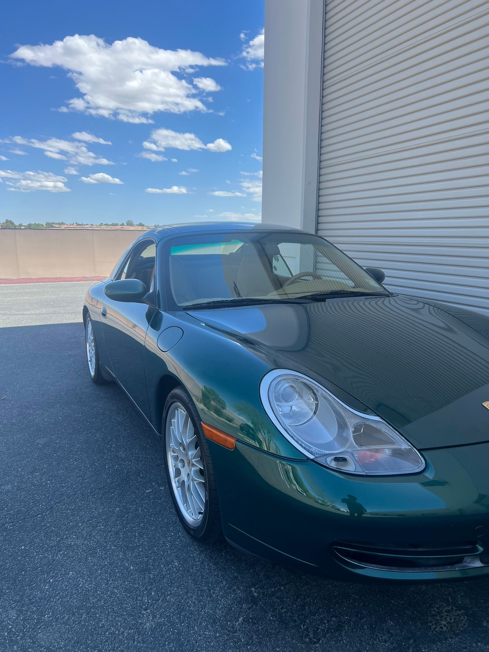 A green porsche 911 is parked in front of a garage door.