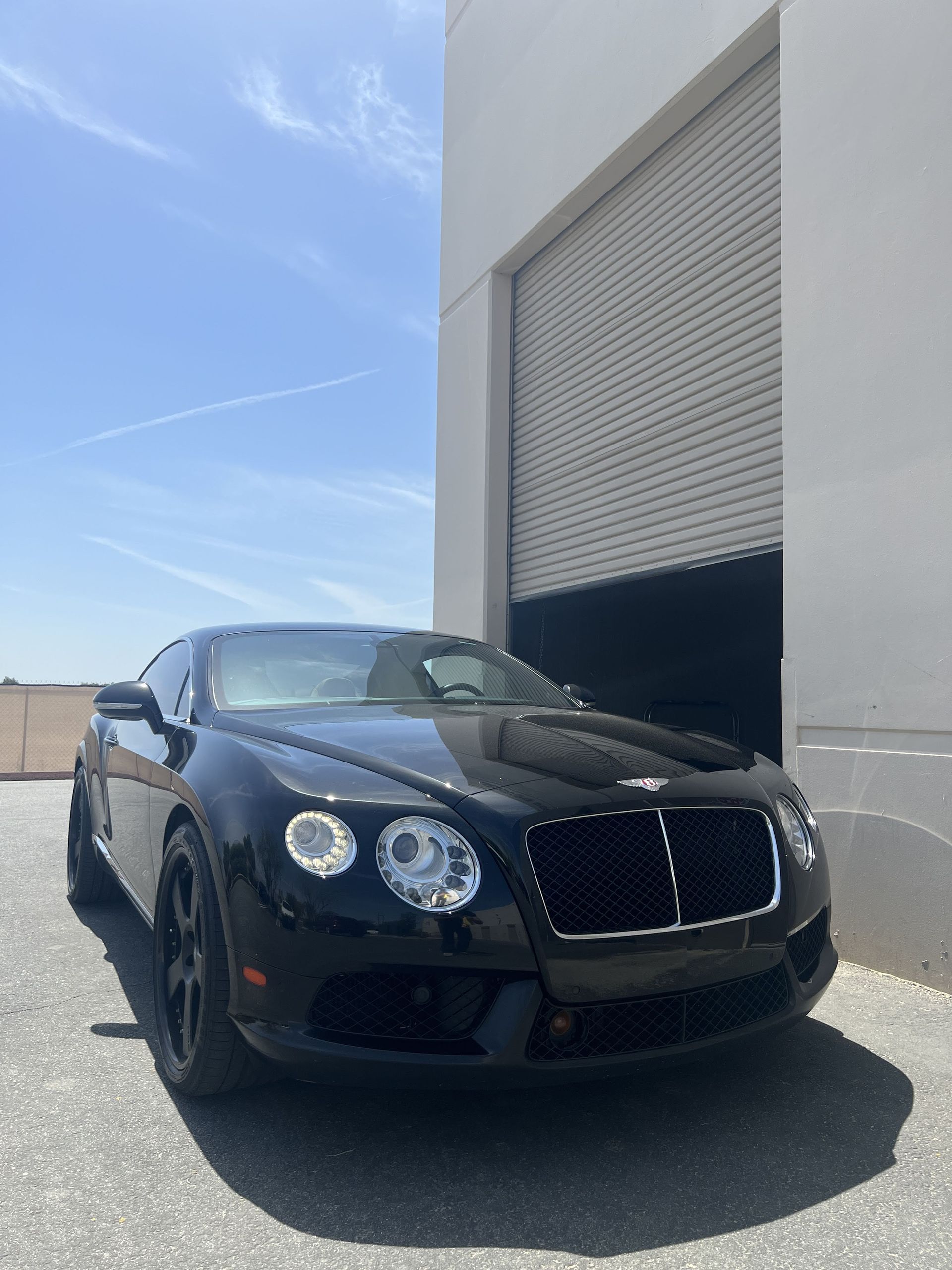 A black bentley is parked in front of a garage door.