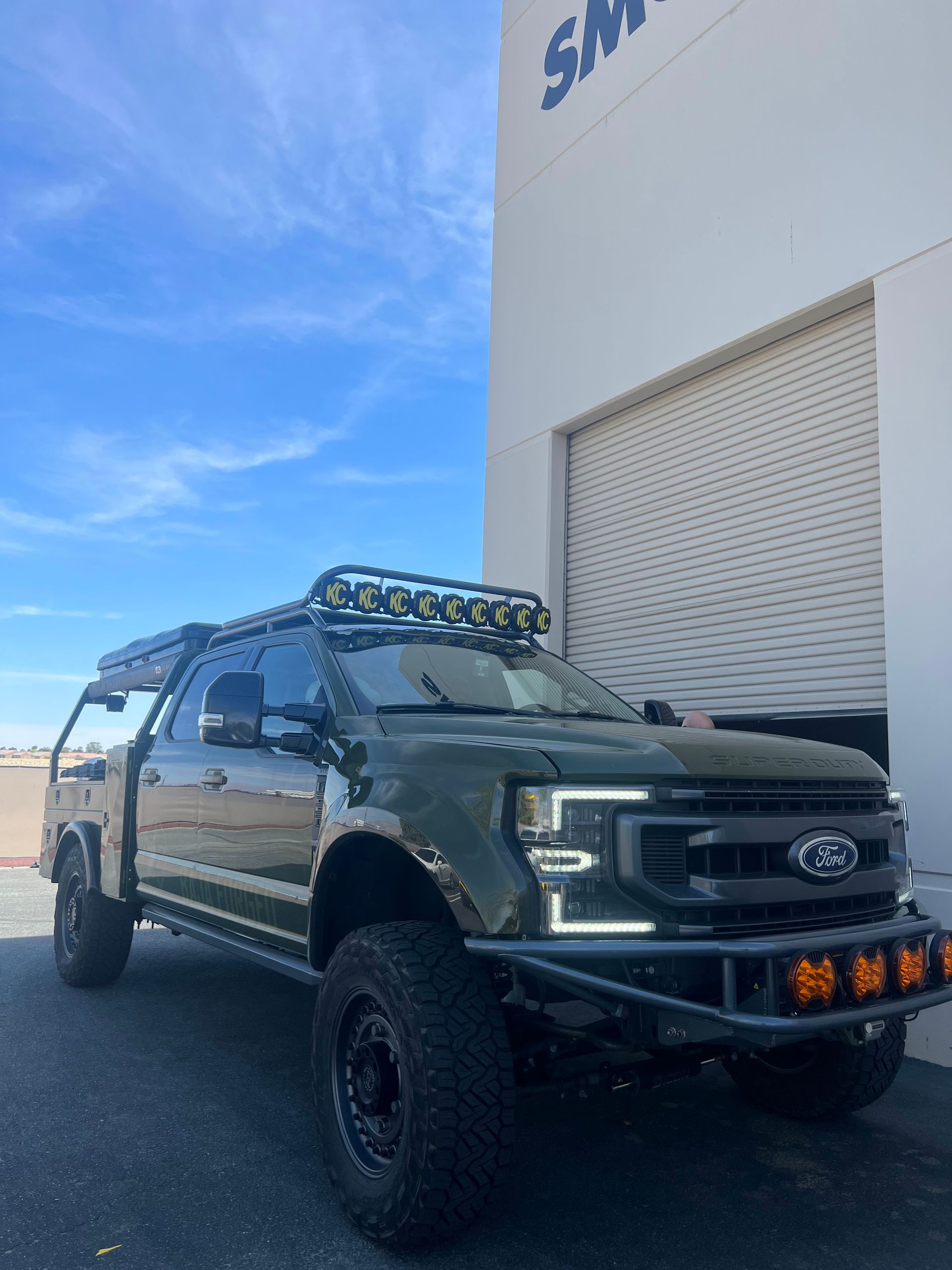 A green ford truck is parked in front of a building.
