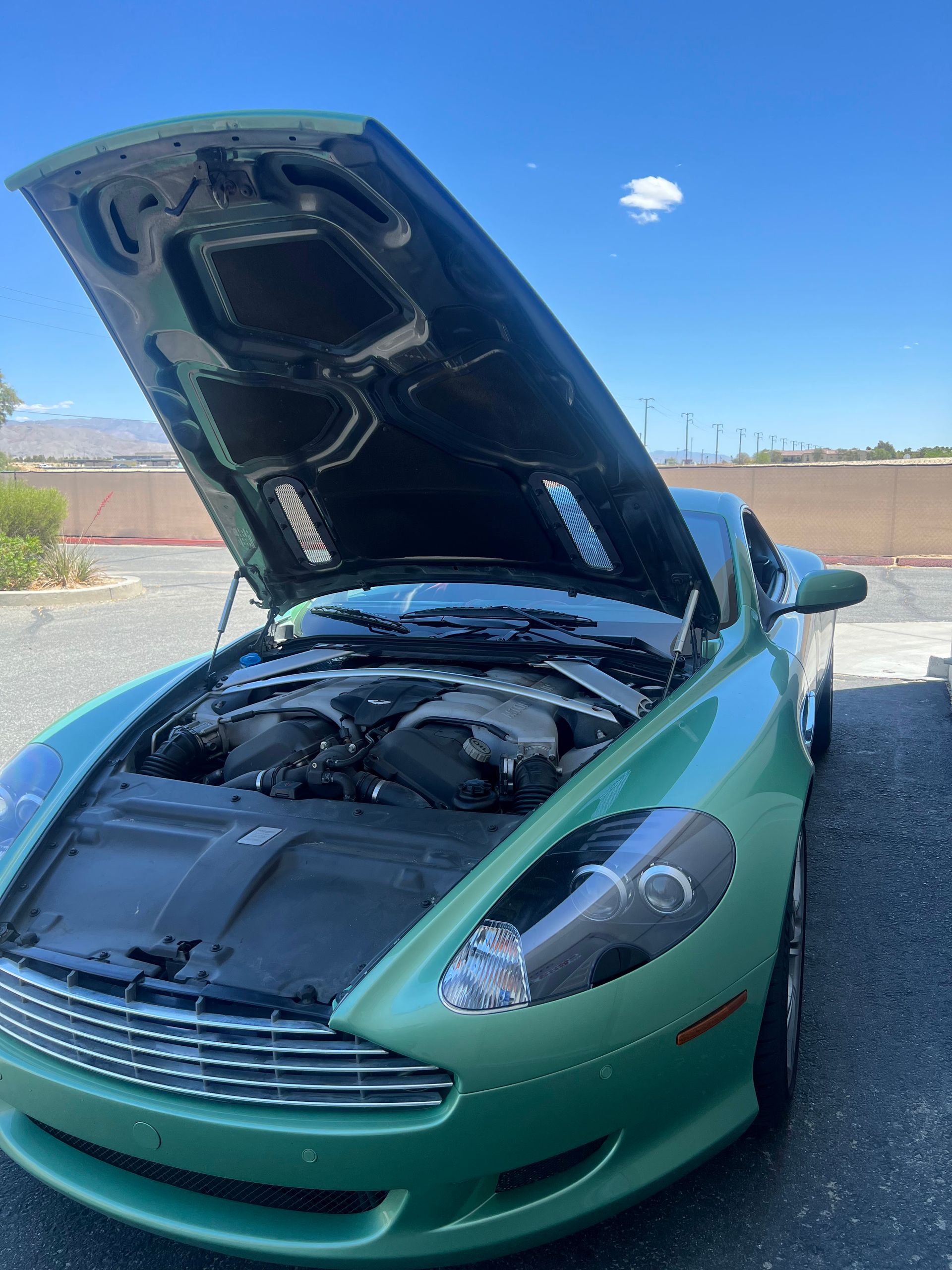 A green sports car with the hood up is parked in a parking lot.