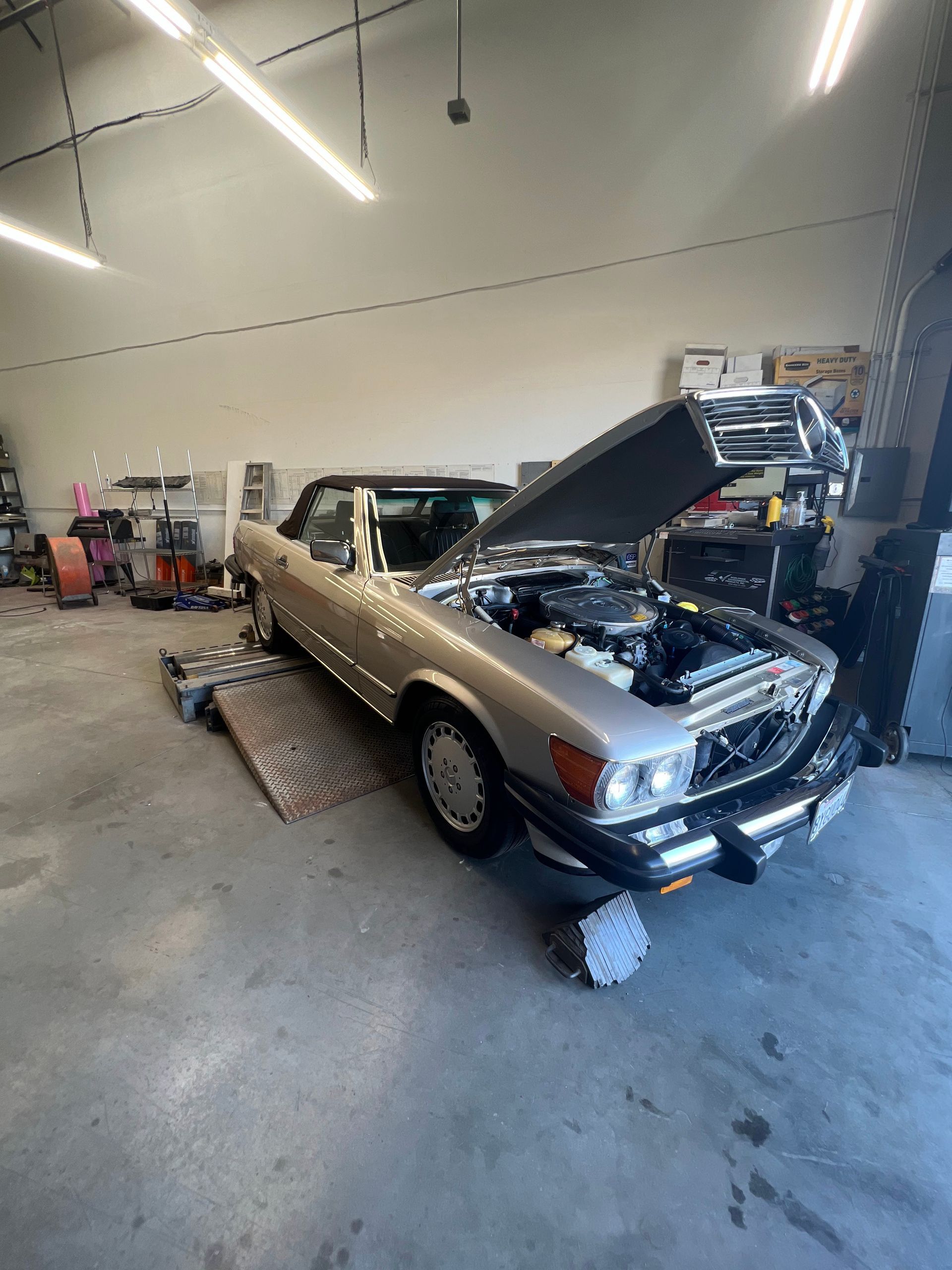 A silver car with the hood up is parked in a garage.