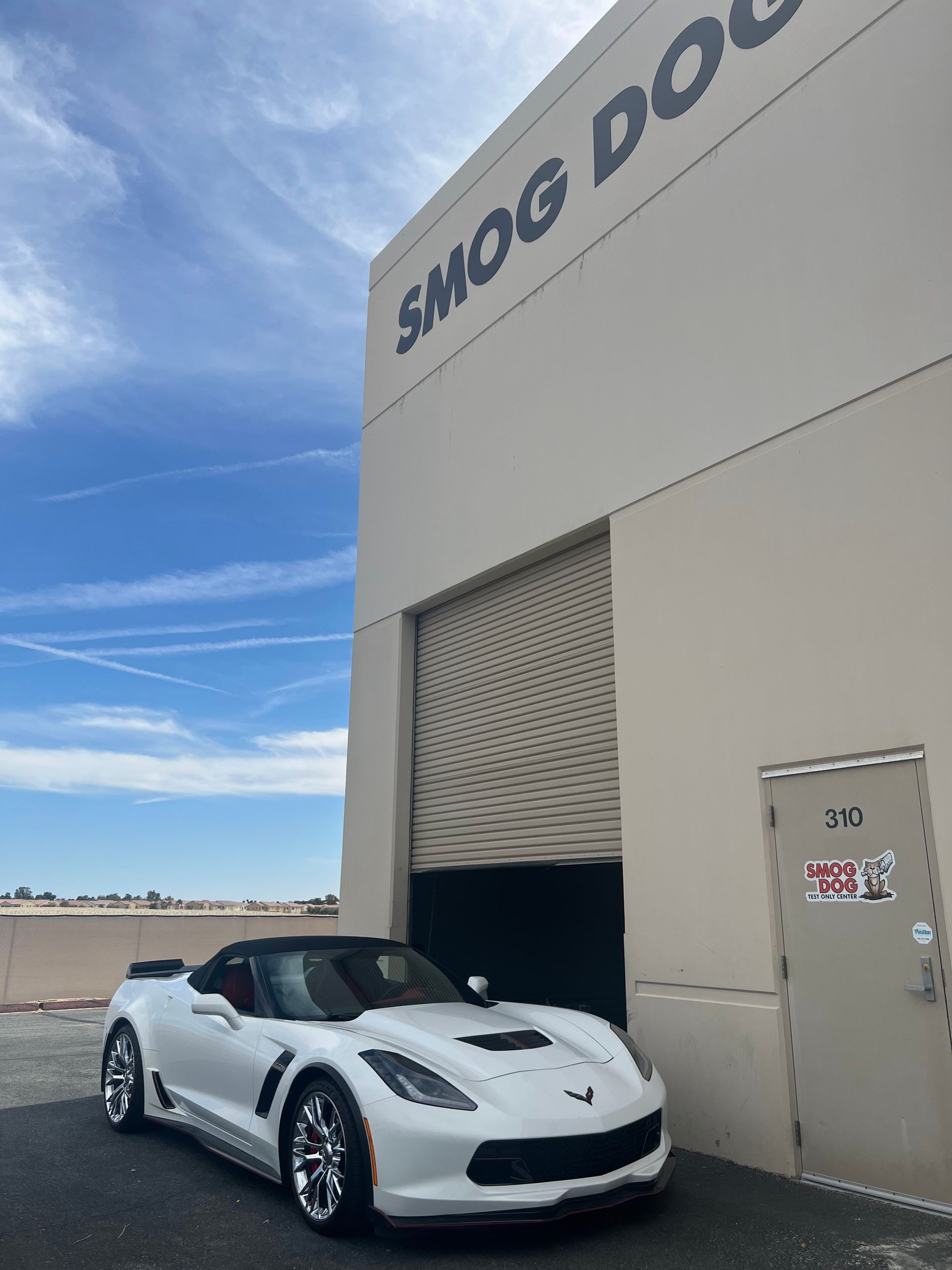 A white sports car is parked in front of a building that says smog dog