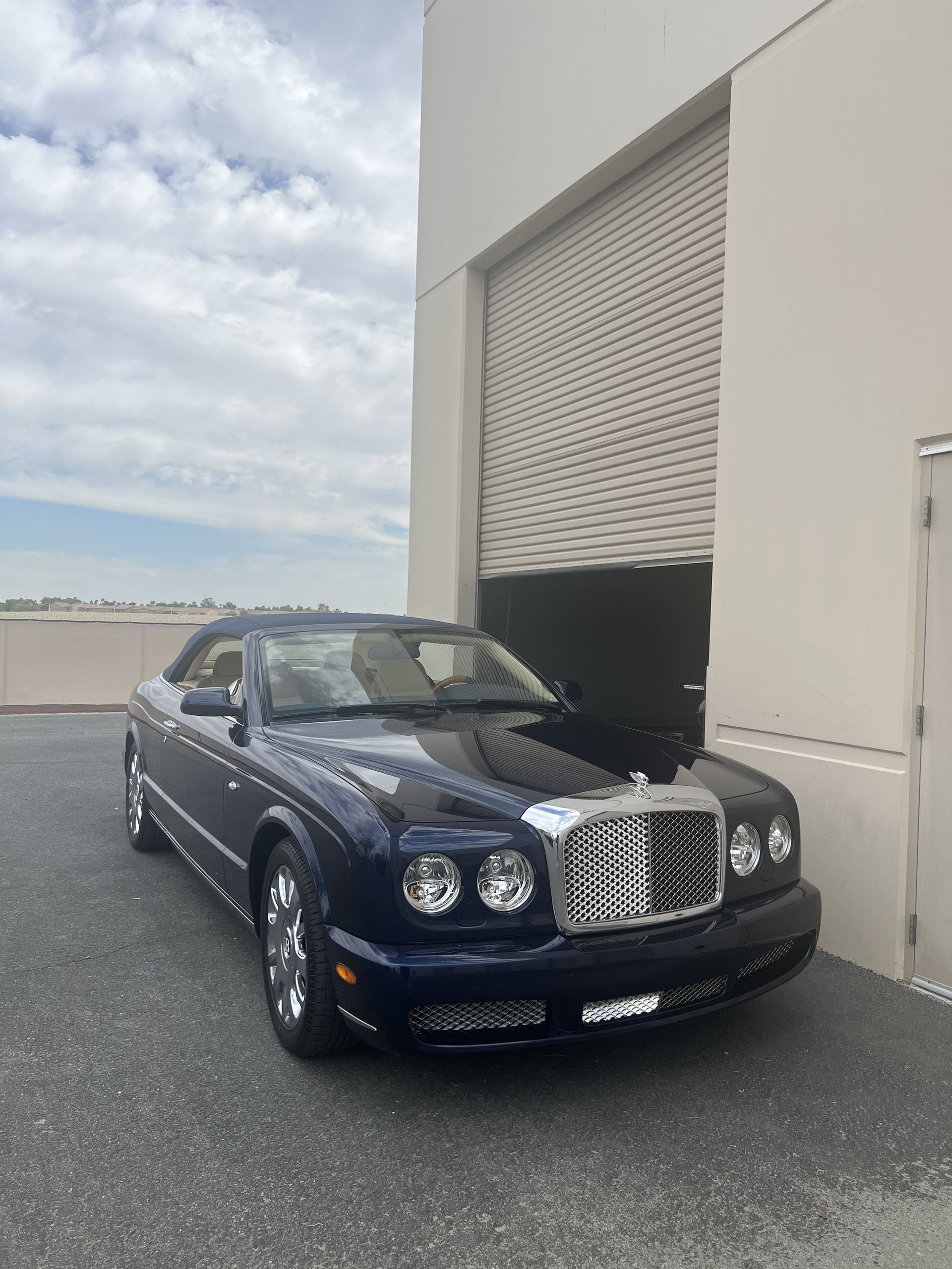 A blue bentley convertible is parked in front of a building.