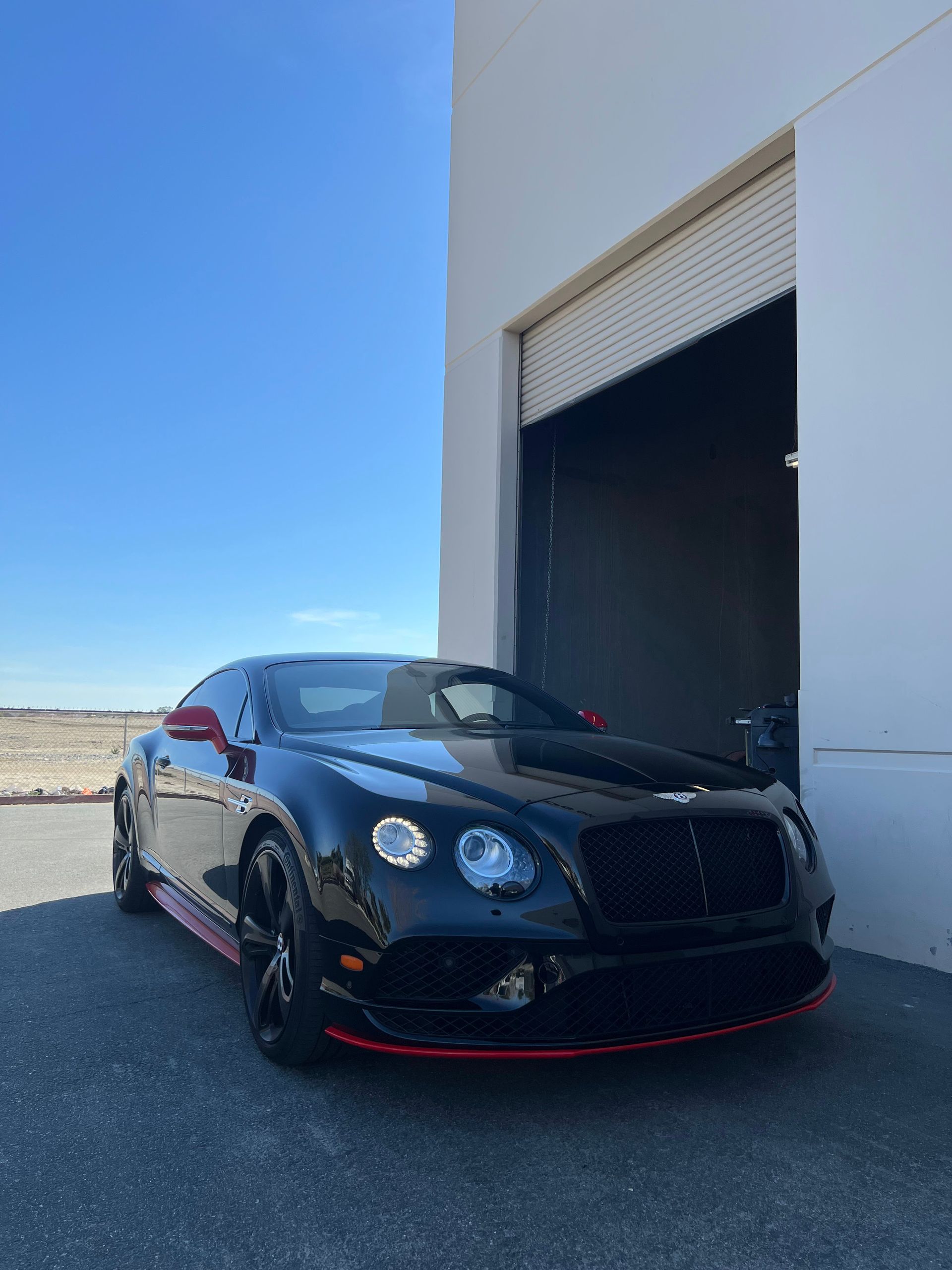 A black bentley is parked in front of a garage door.