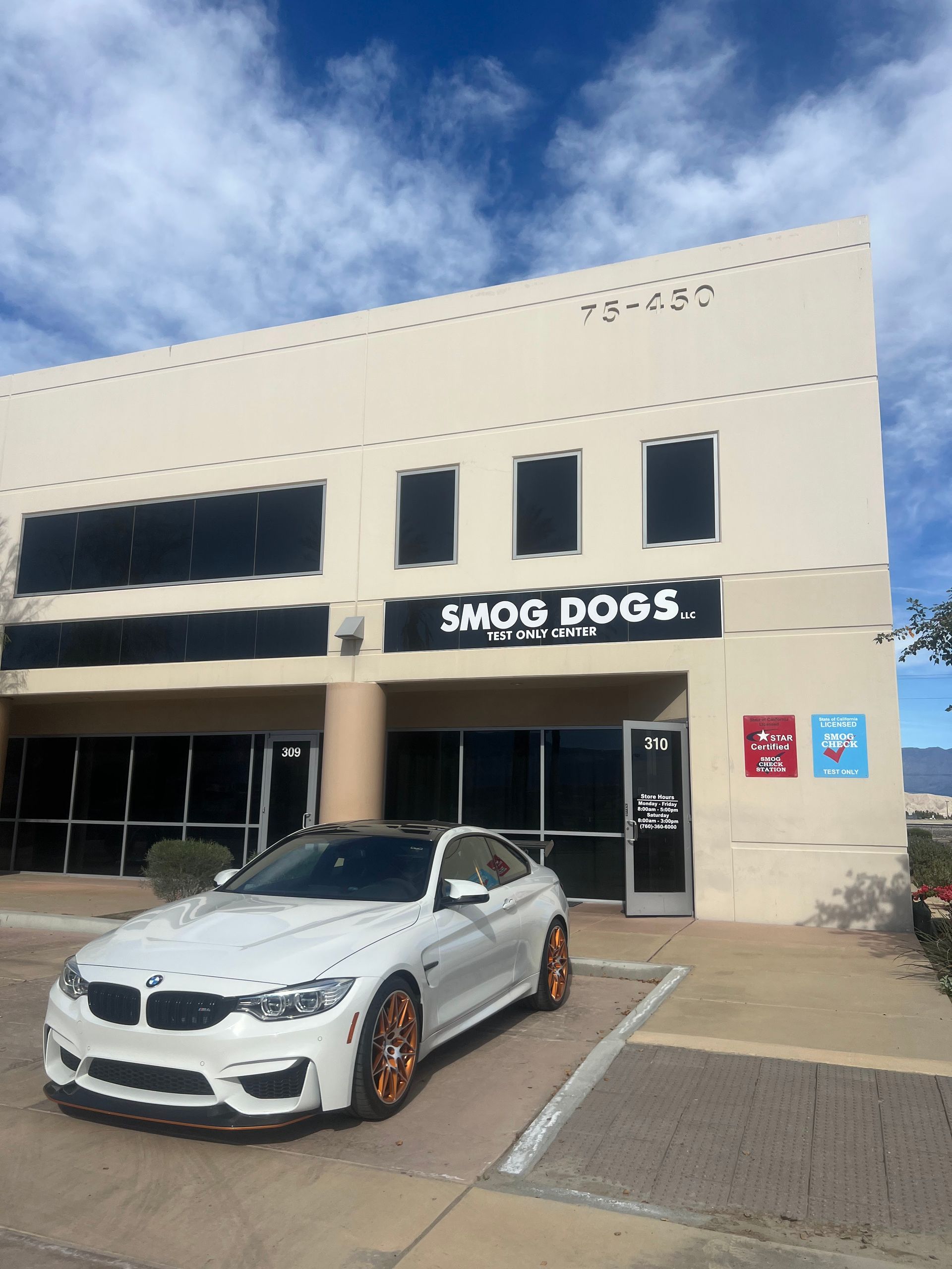 A white car is parked in front of a building that says smog dogs
