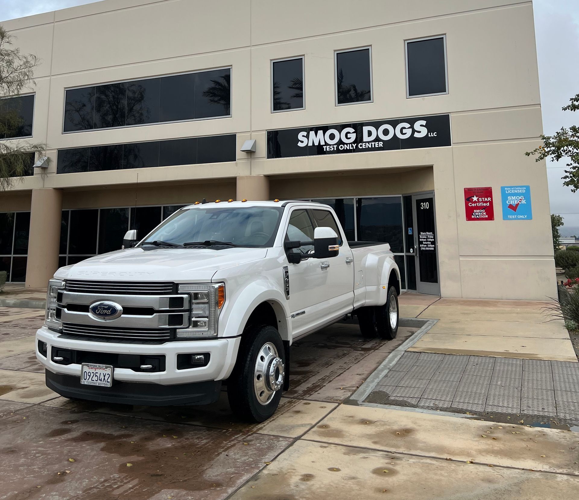 A white truck is parked in front of a building that says smog dogs