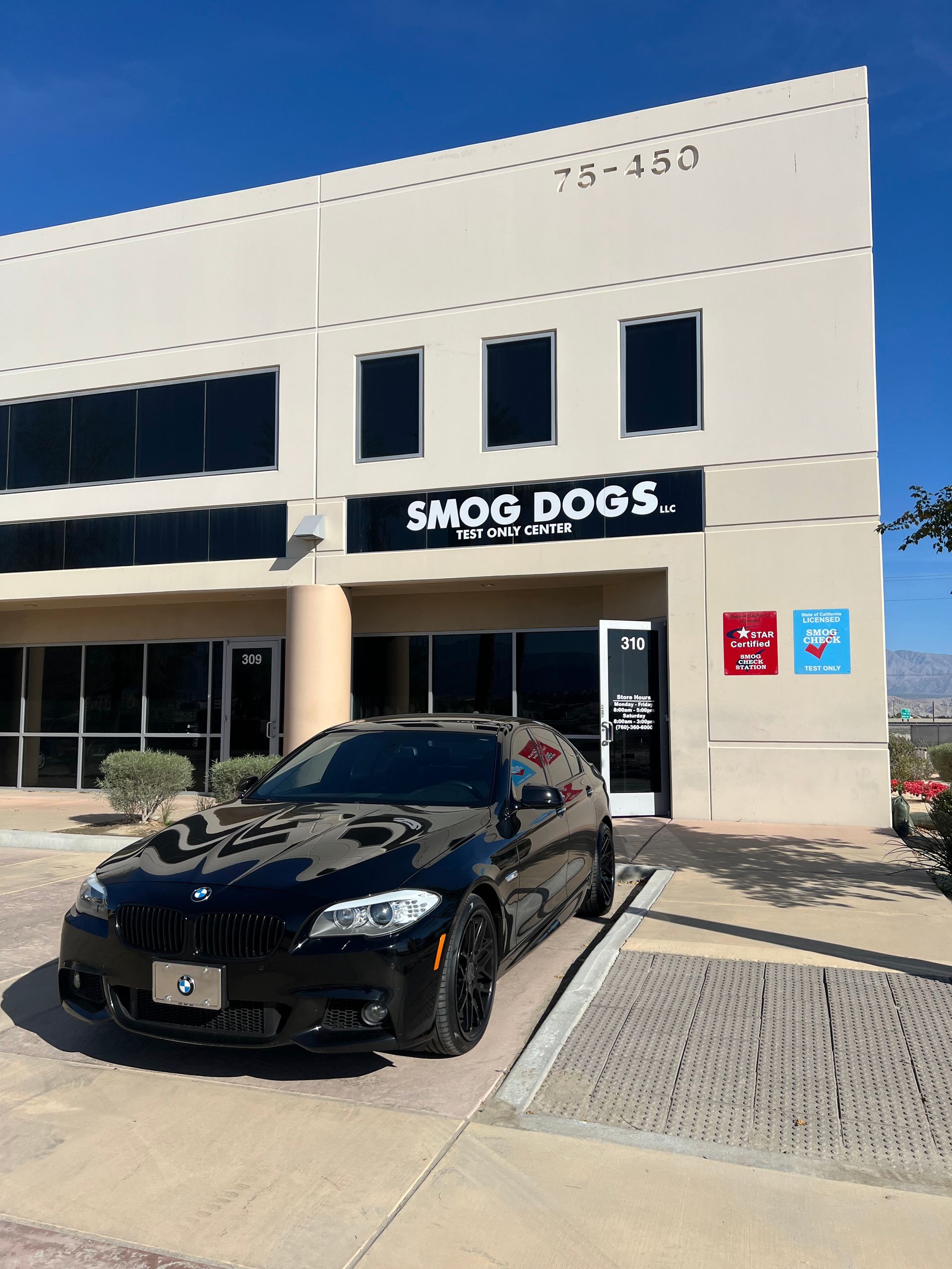 A black car is parked in front of a building that says smog dogs