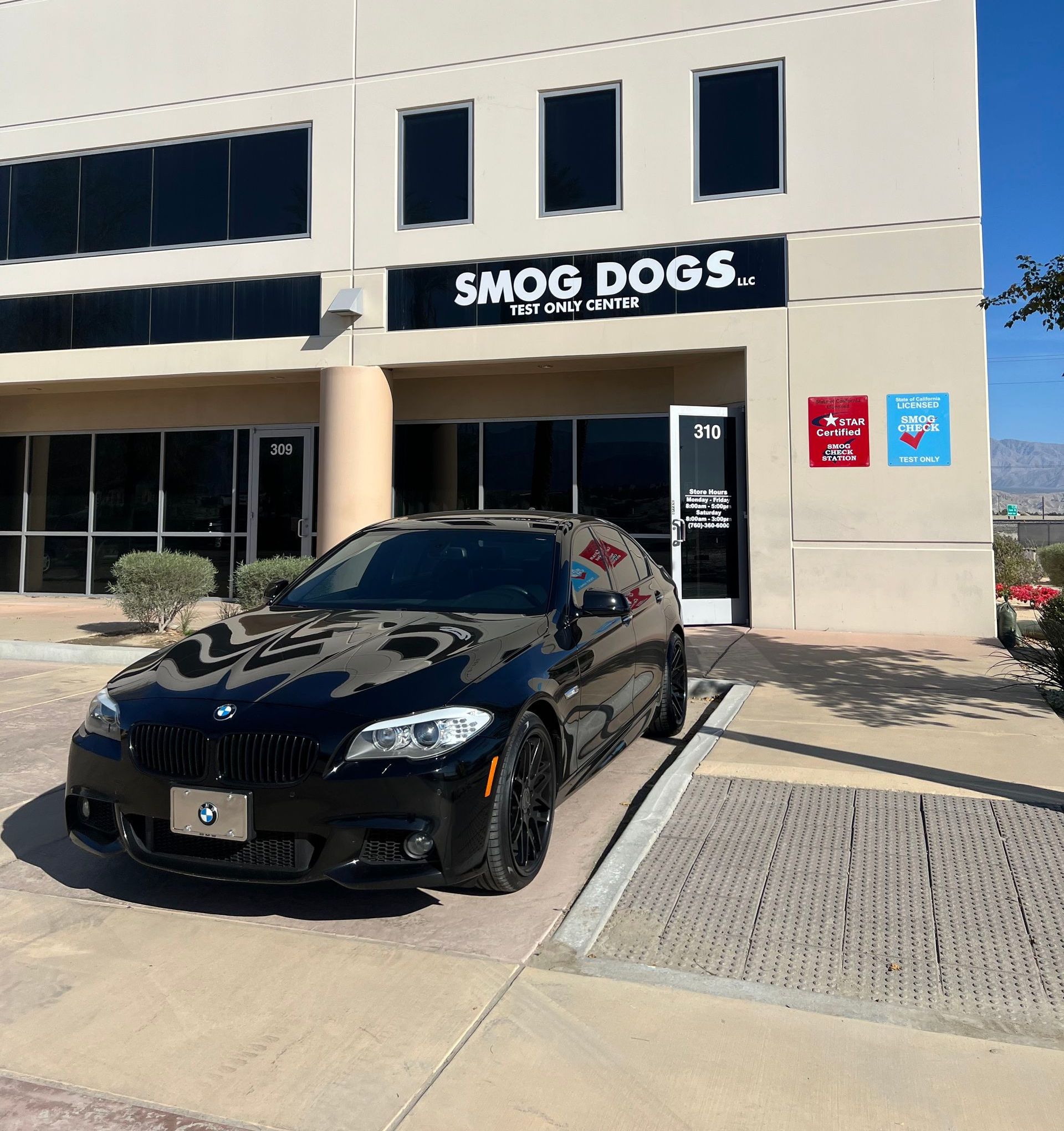 A black car is parked in front of a building that says smog dogs